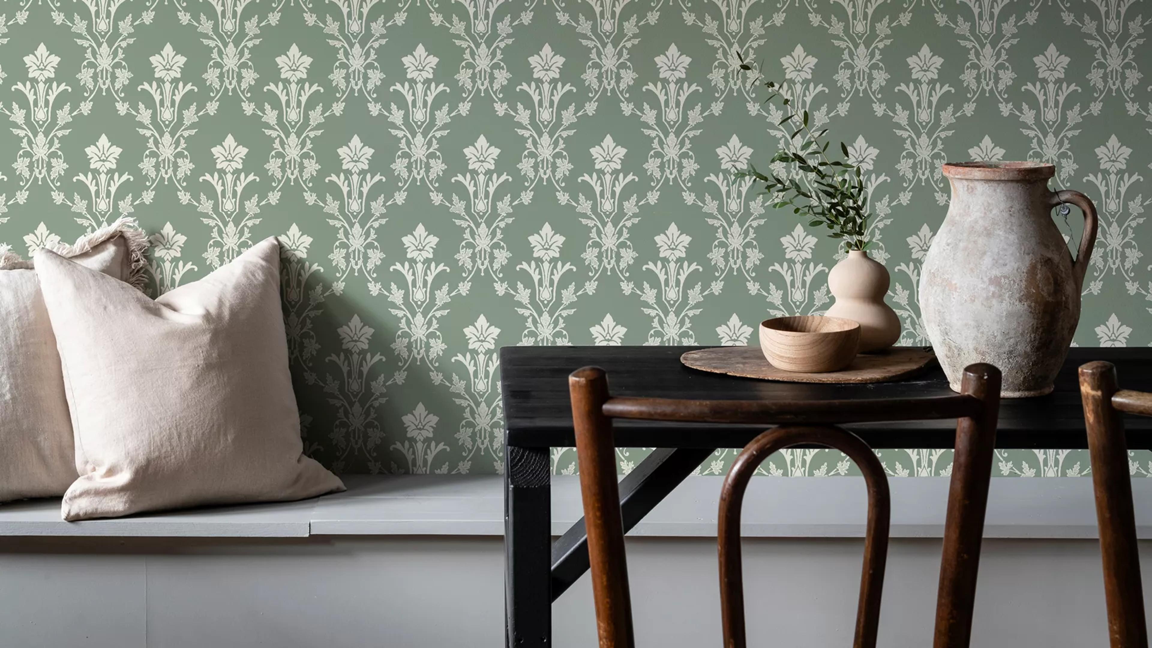 Sage green wallpaper with a cream damask pattern, a bench with pillows, and a table with rustic pottery.