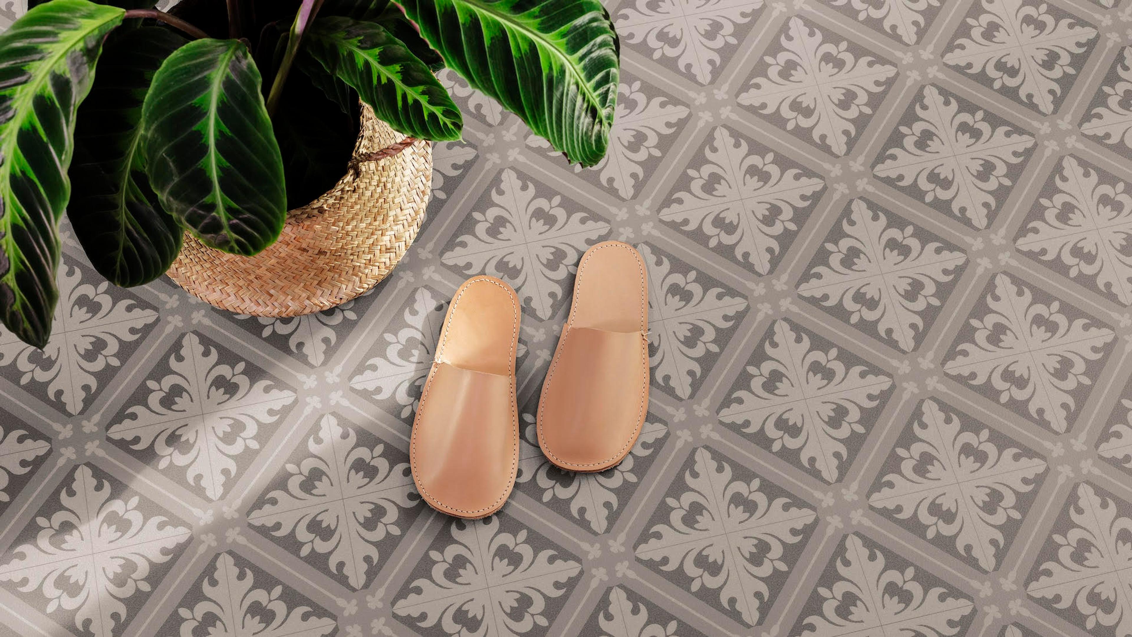 Tan slippers on a grey and white patterned tile floor next to a potted plant.