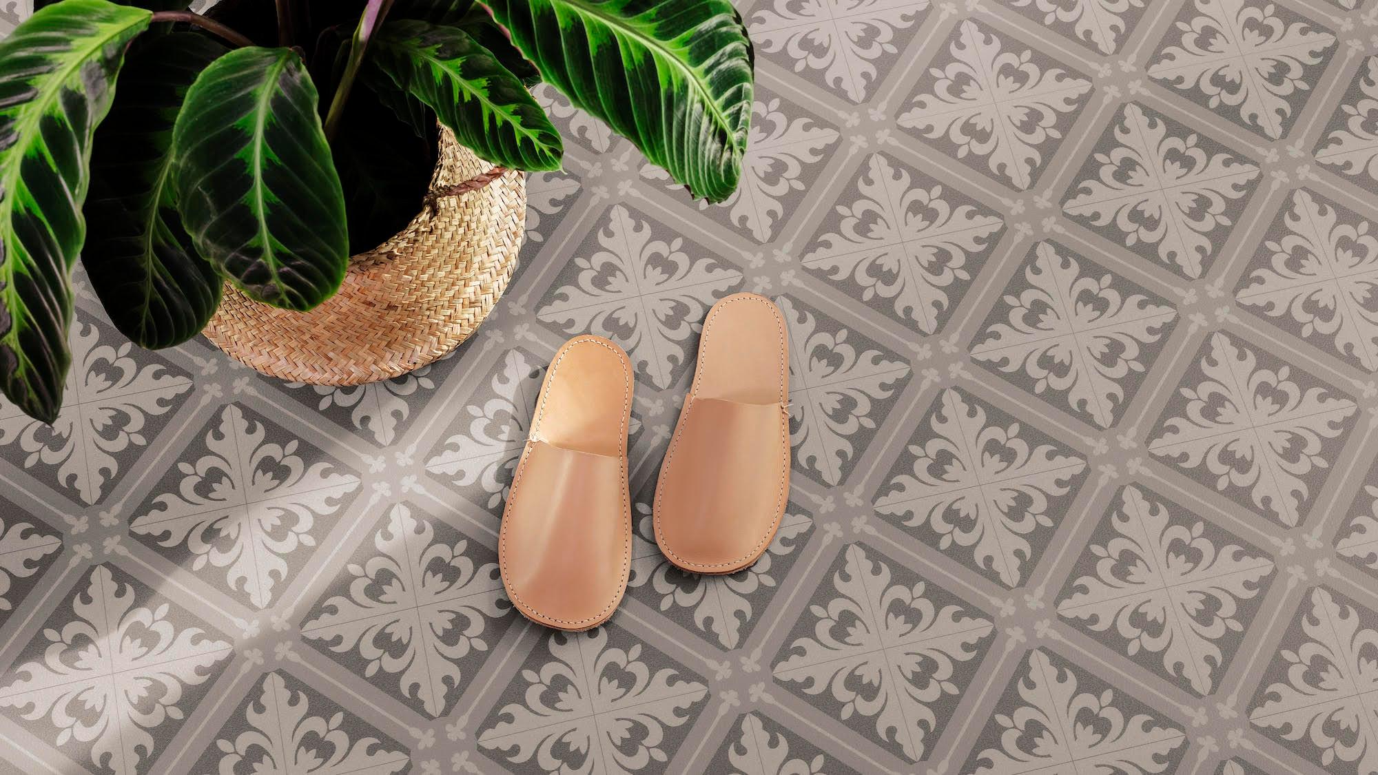 Tan slippers on a grey and white patterned tile floor next to a potted plant.