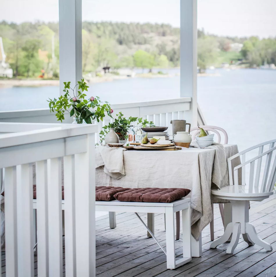 An outdoor dining table set on a white porch overlooking a tranquil lake.