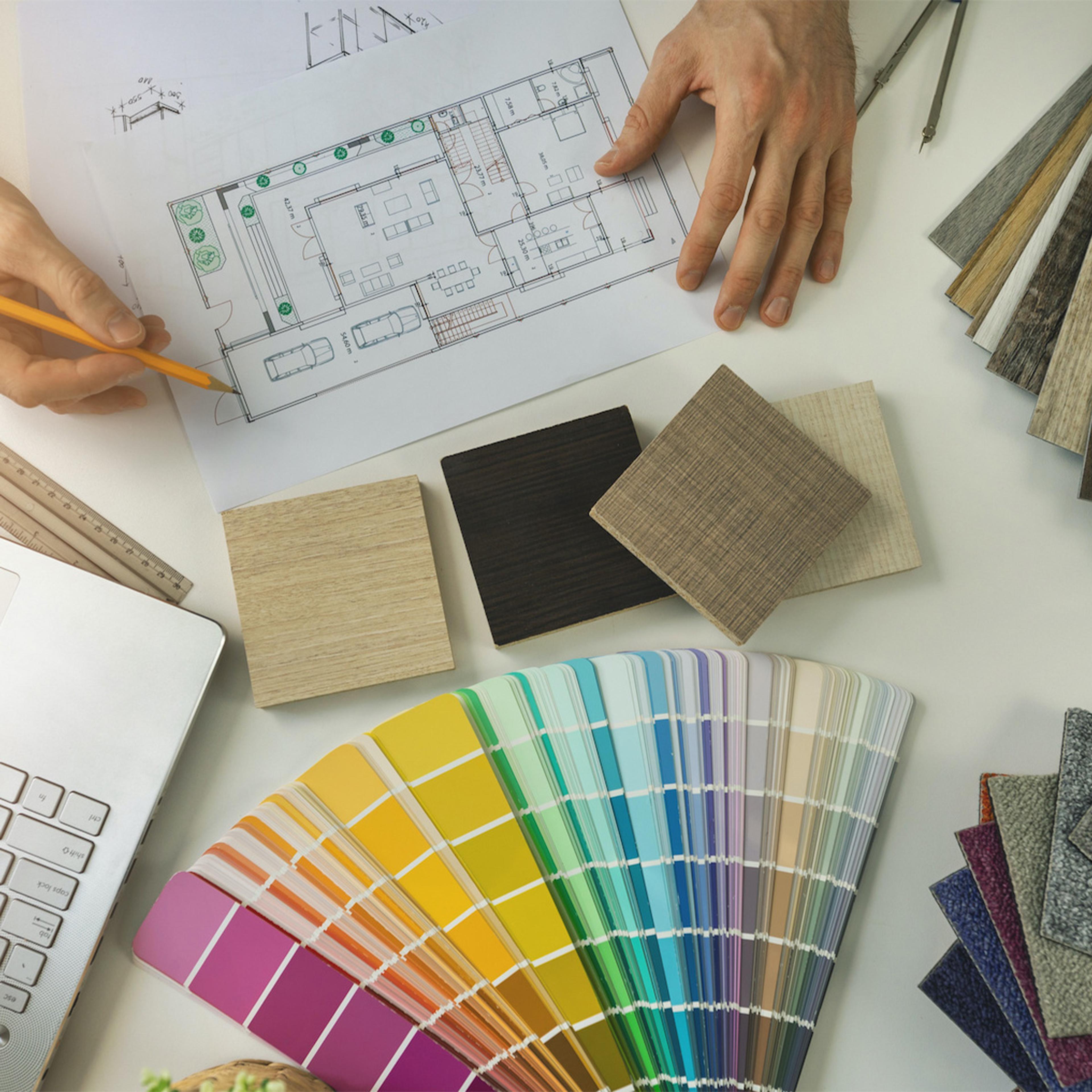 Hands working on a blueprint, surrounded by material and color samples.