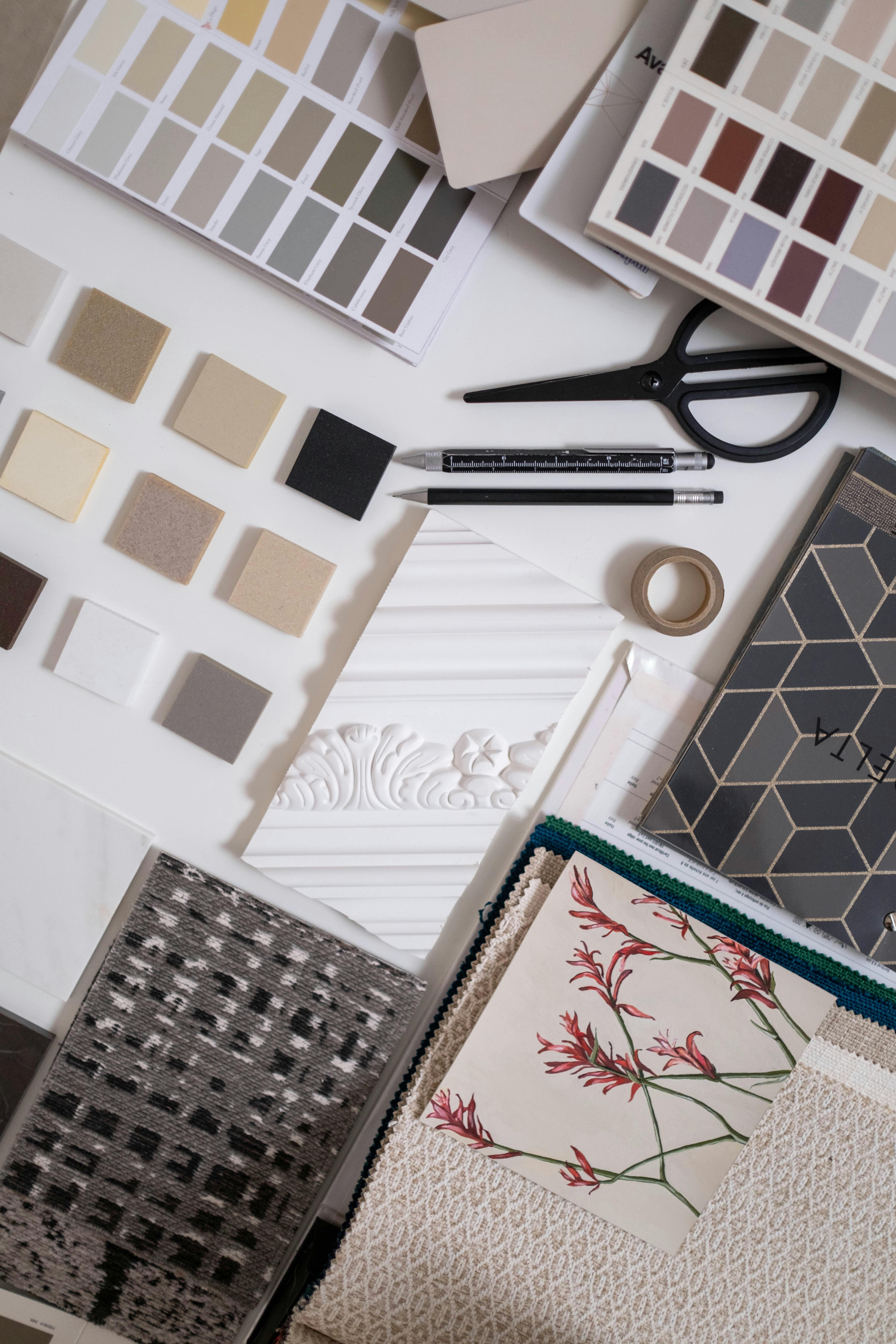 A flat lay of interior design samples including color swatches, material squares, fabric swatches, decorative trim, and design tools.