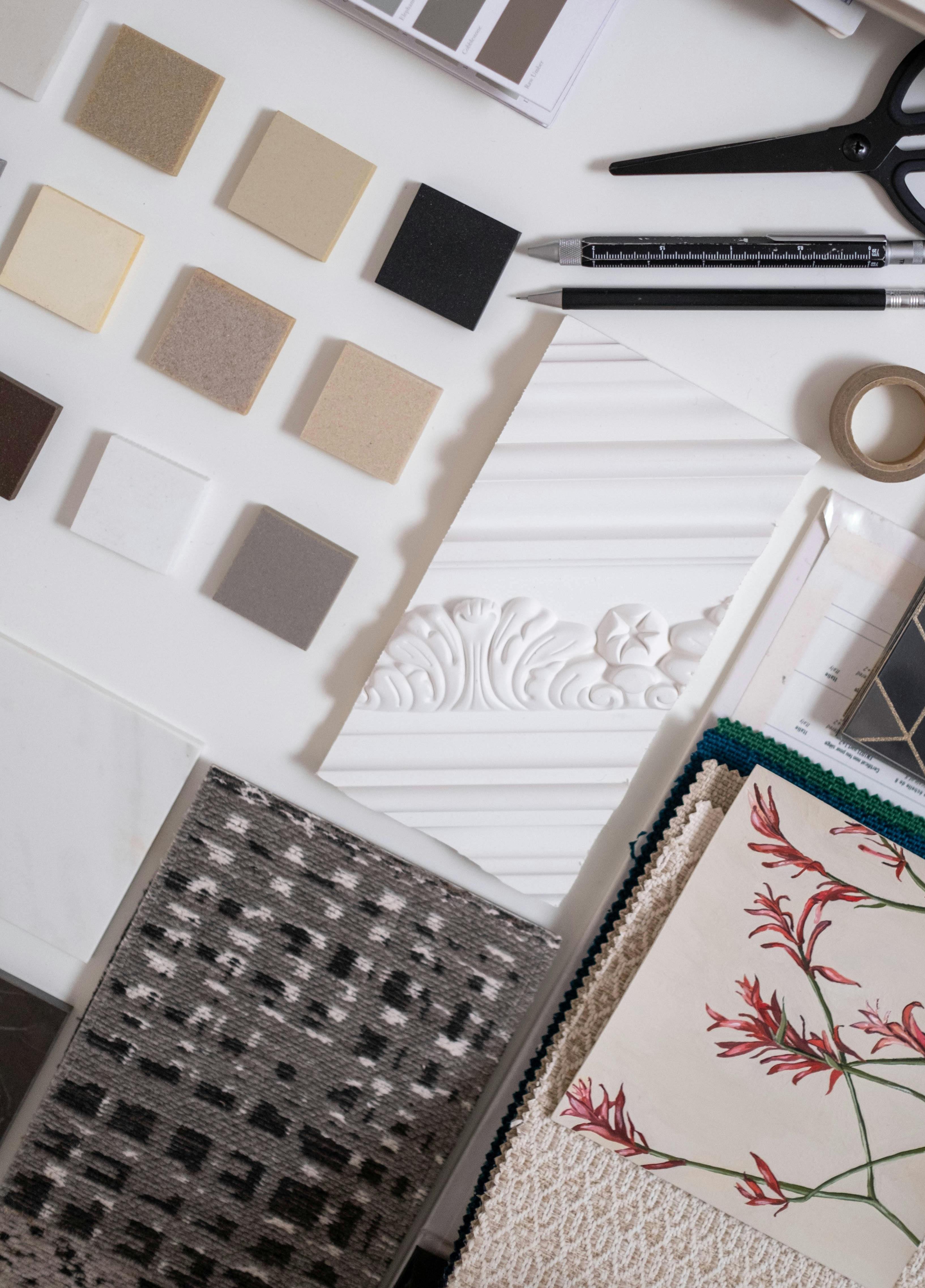 A flat lay of interior design samples including color swatches, material squares, fabric swatches, decorative trim, and design tools.