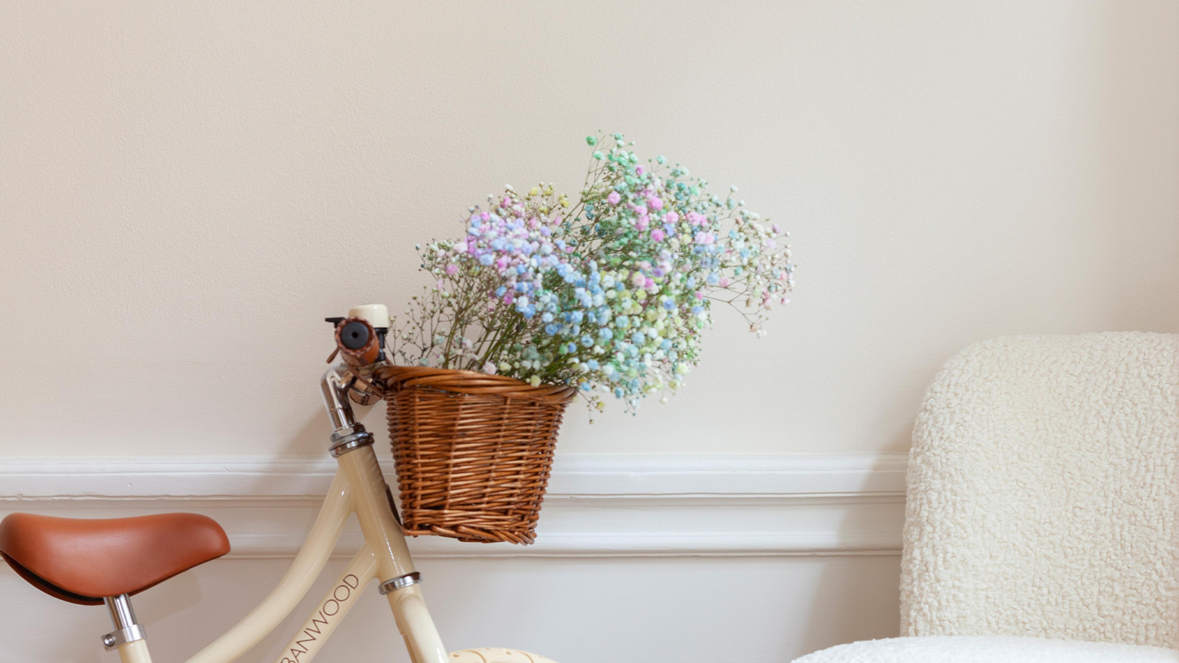 Cream bicycle with a wicker basket filled with colorful baby's breath, next to a cream chair.