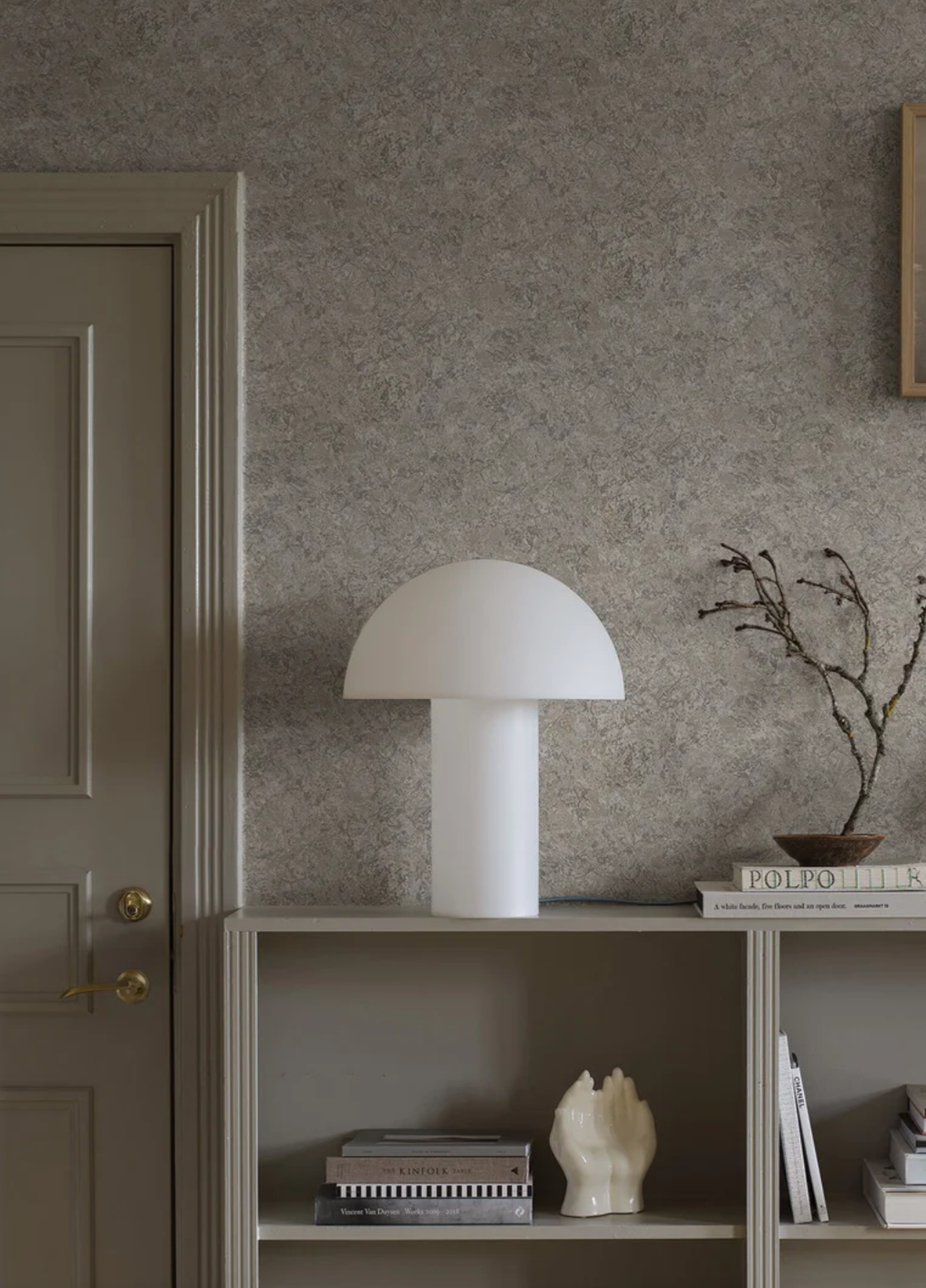 A white mushroom-shaped lamp on a grey shelf, with a matching door and textured grey wallpaper in the background.