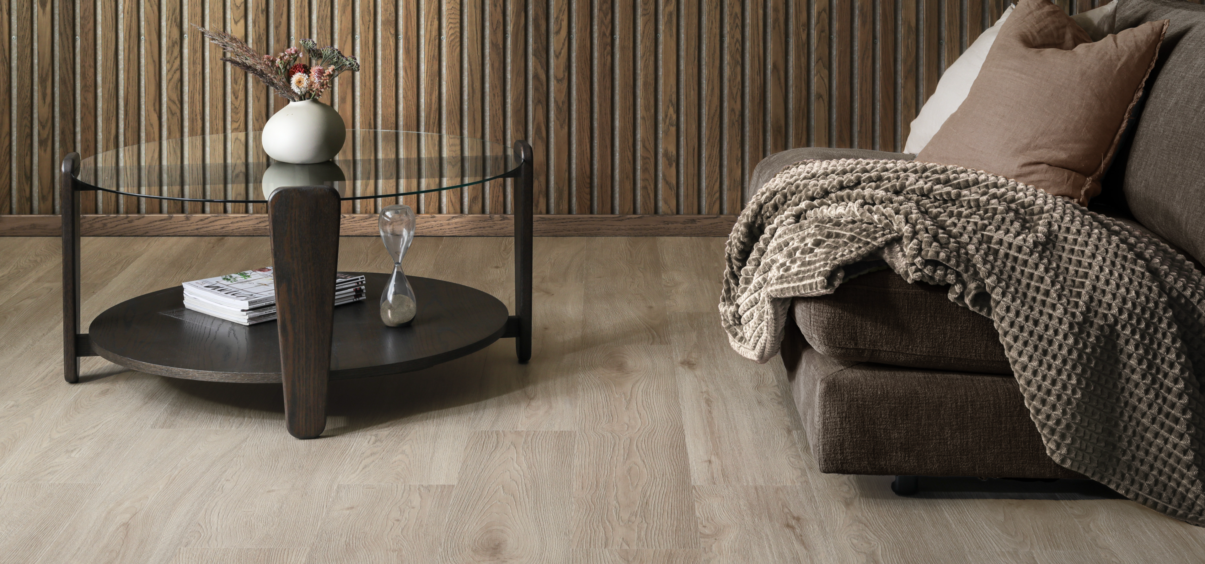 Living room with a dark wood coffee table, brown sofa, light wood floor, and slatted wood wall.