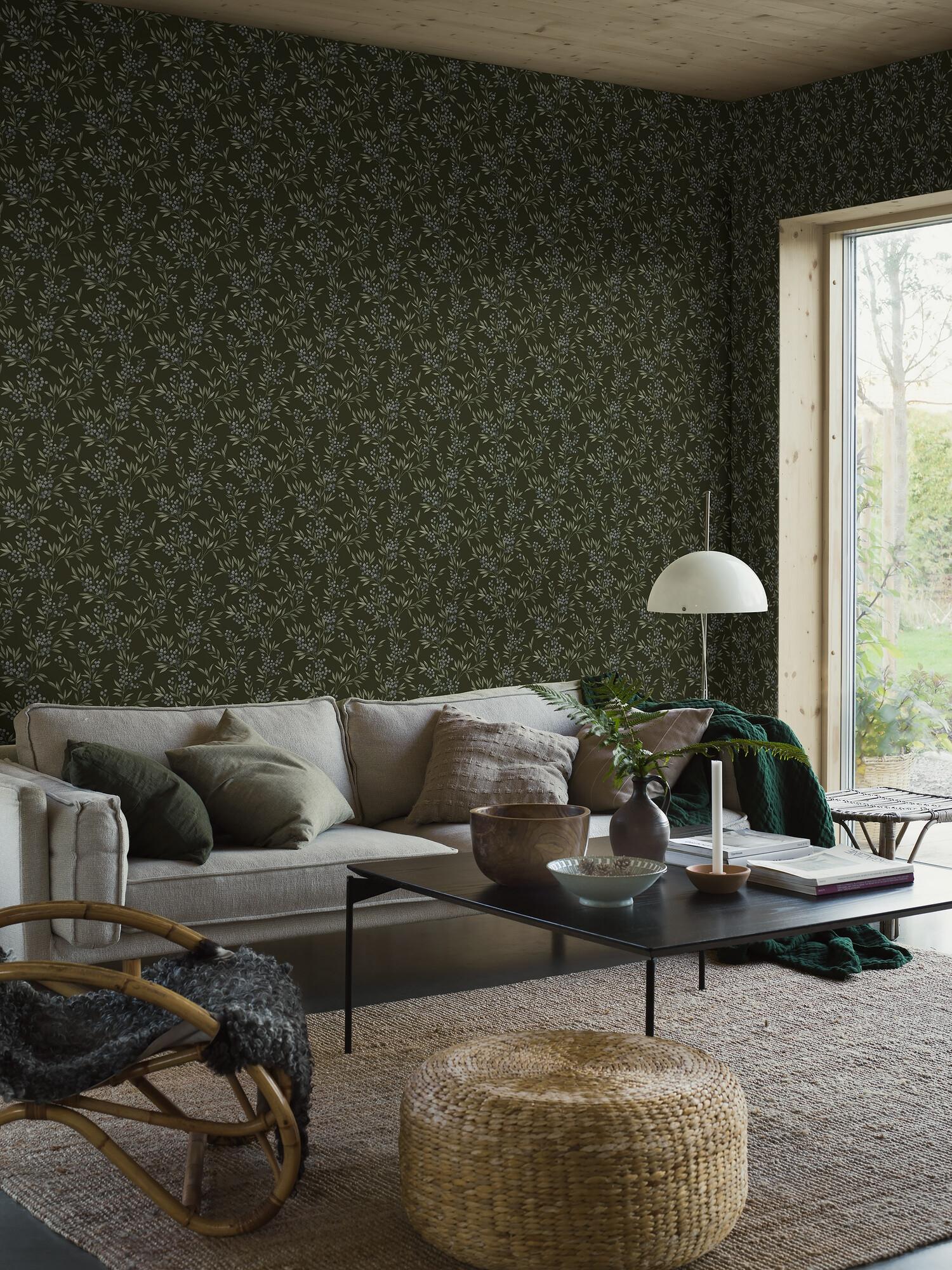 A cozy living room with dark green botanical wallpaper, a light sofa, natural fiber rug, and wooden ceiling.