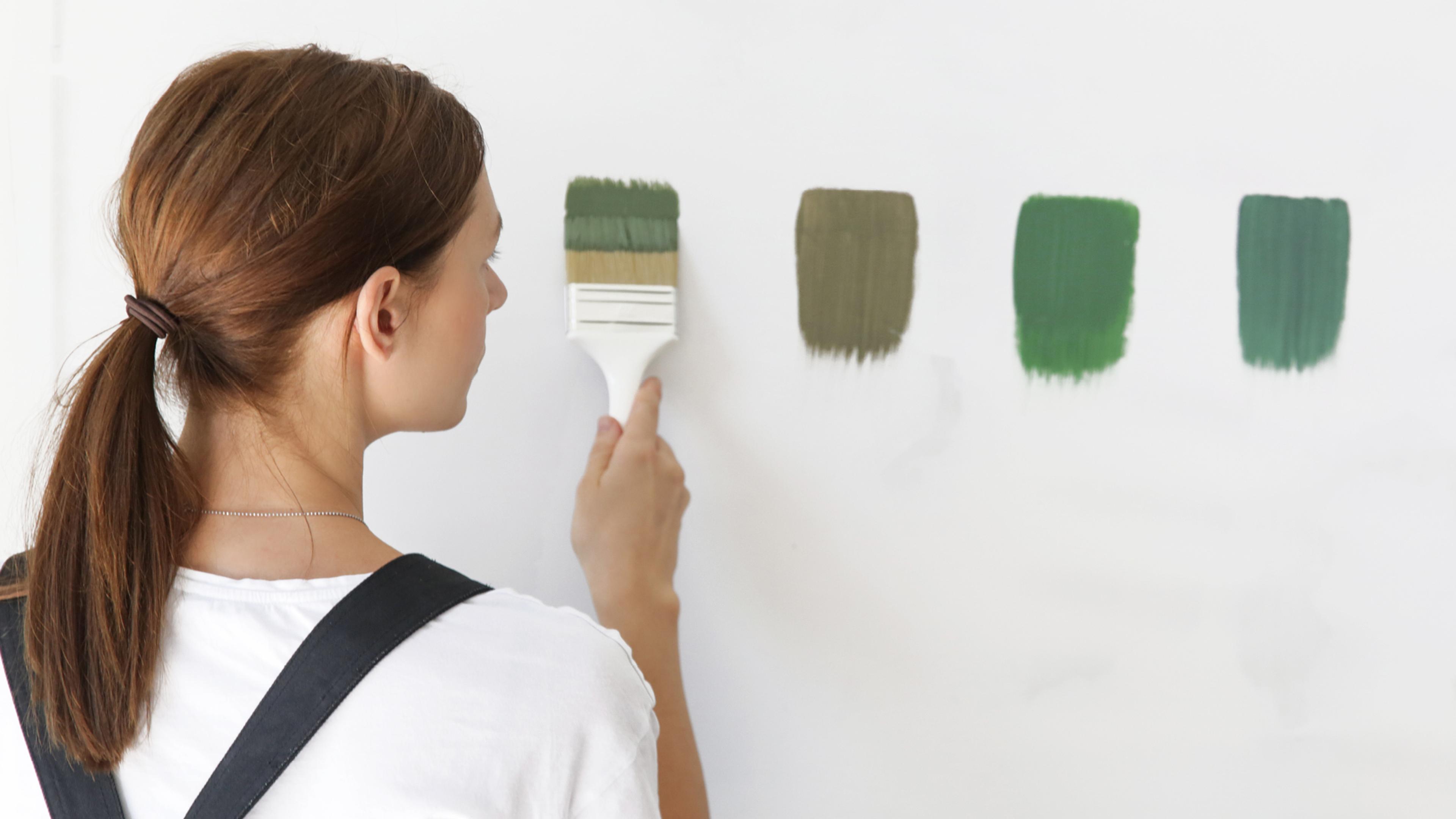 Woman painting green swatches on a white wall.