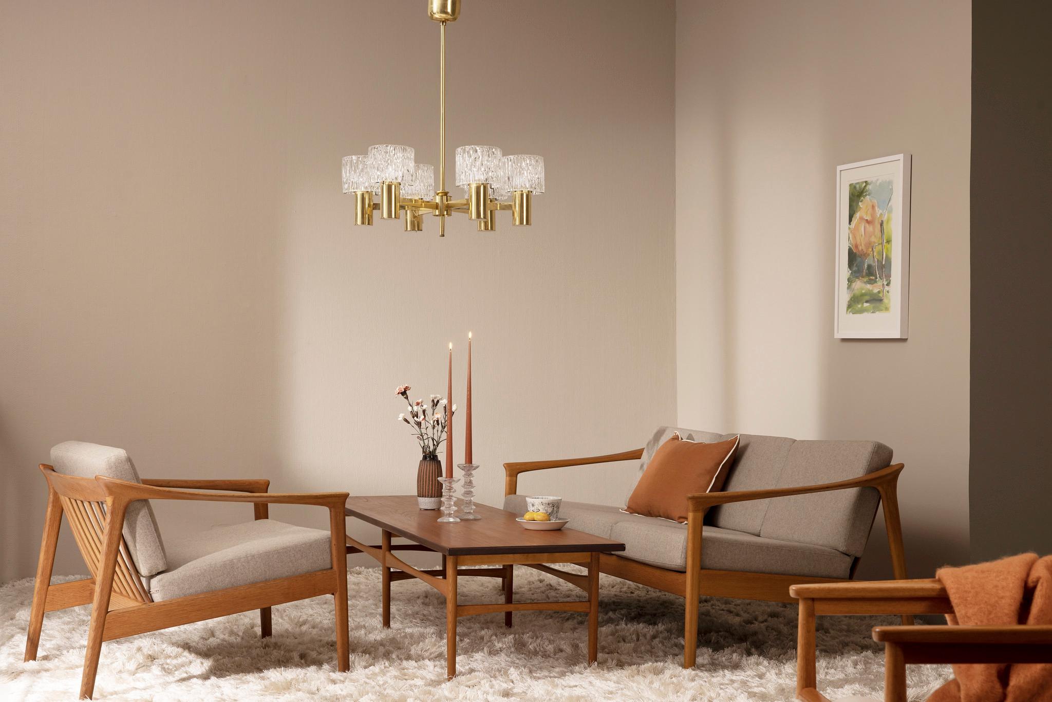 Mid-century modern living room with a brass and glass chandelier, light wood sofa and armchairs, a coffee table, and a shaggy white rug.