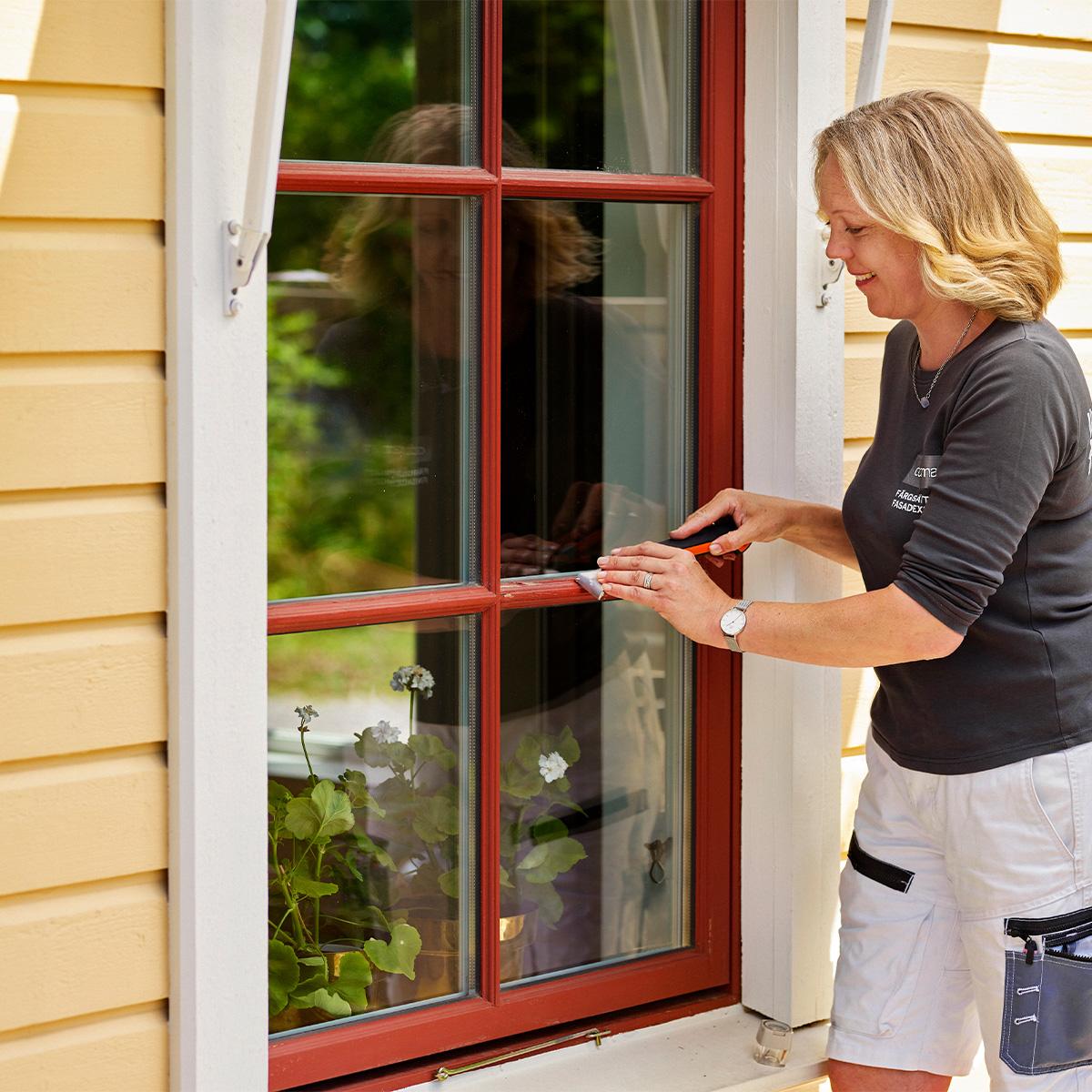 A smiling woman cleans a red-framed window.