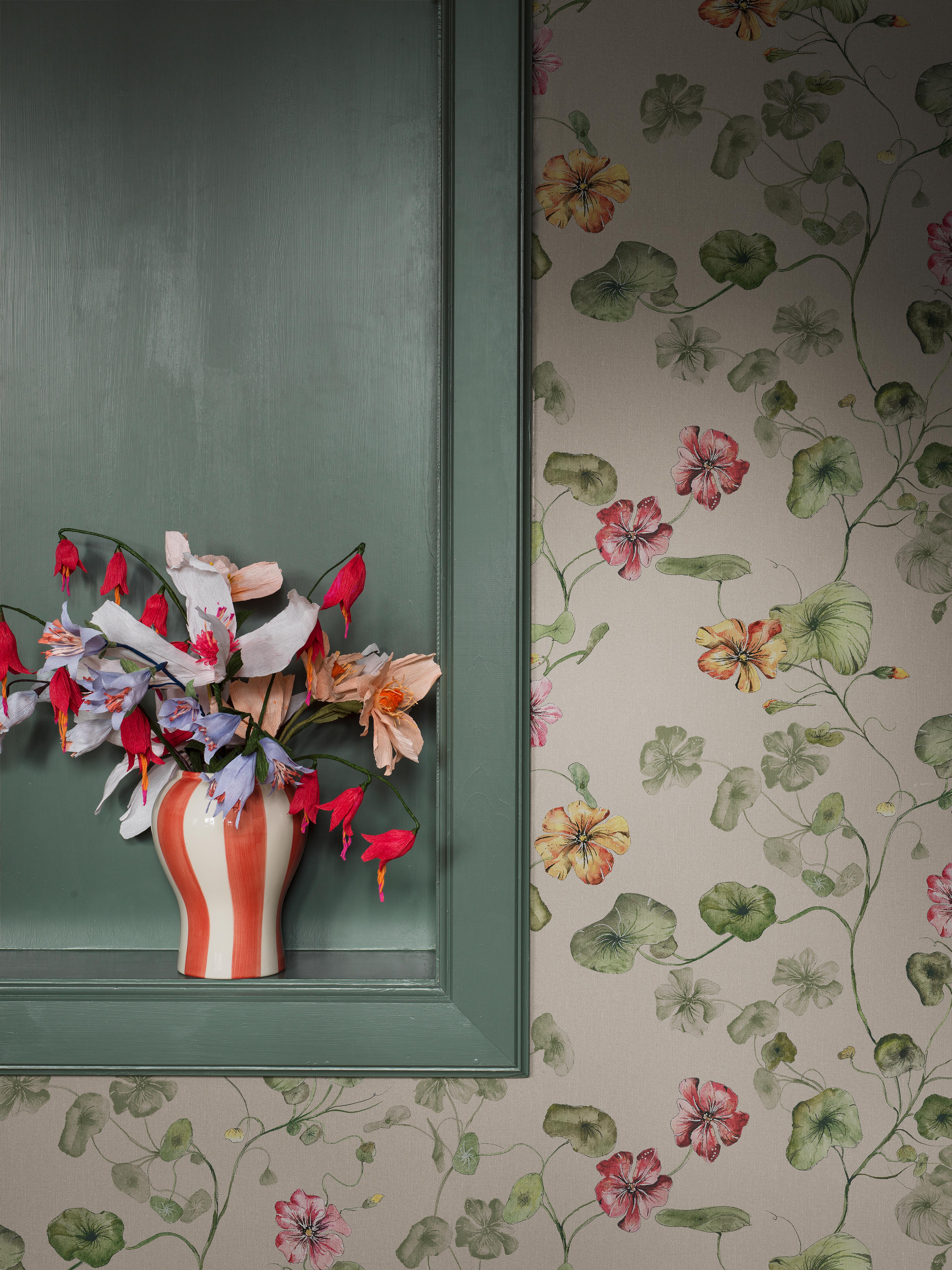 A striped vase with colorful flowers sits in a teal wall niche next to floral wallpaper with leaves and blooms.