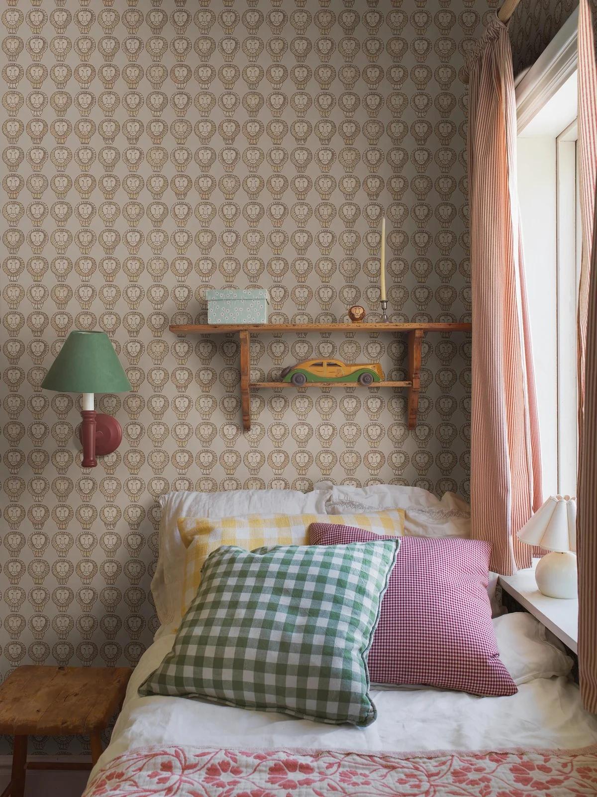A cozy bedroom with lion-patterned wallpaper, a bed with colorful gingham pillows, and a wooden shelf.