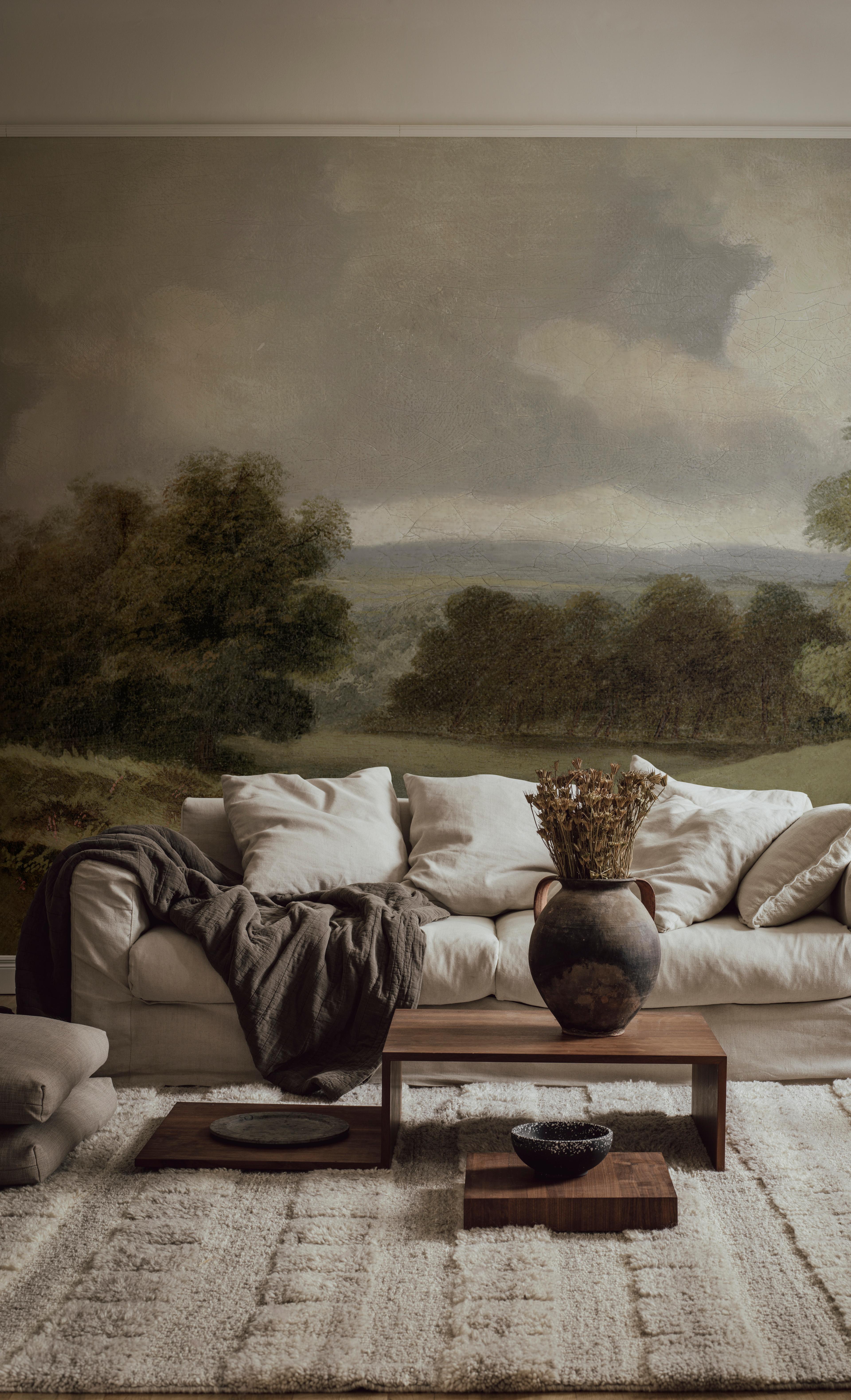 A cozy living room with a large classical landscape mural behind a cream sofa, a wooden coffee table, and a light textured rug.