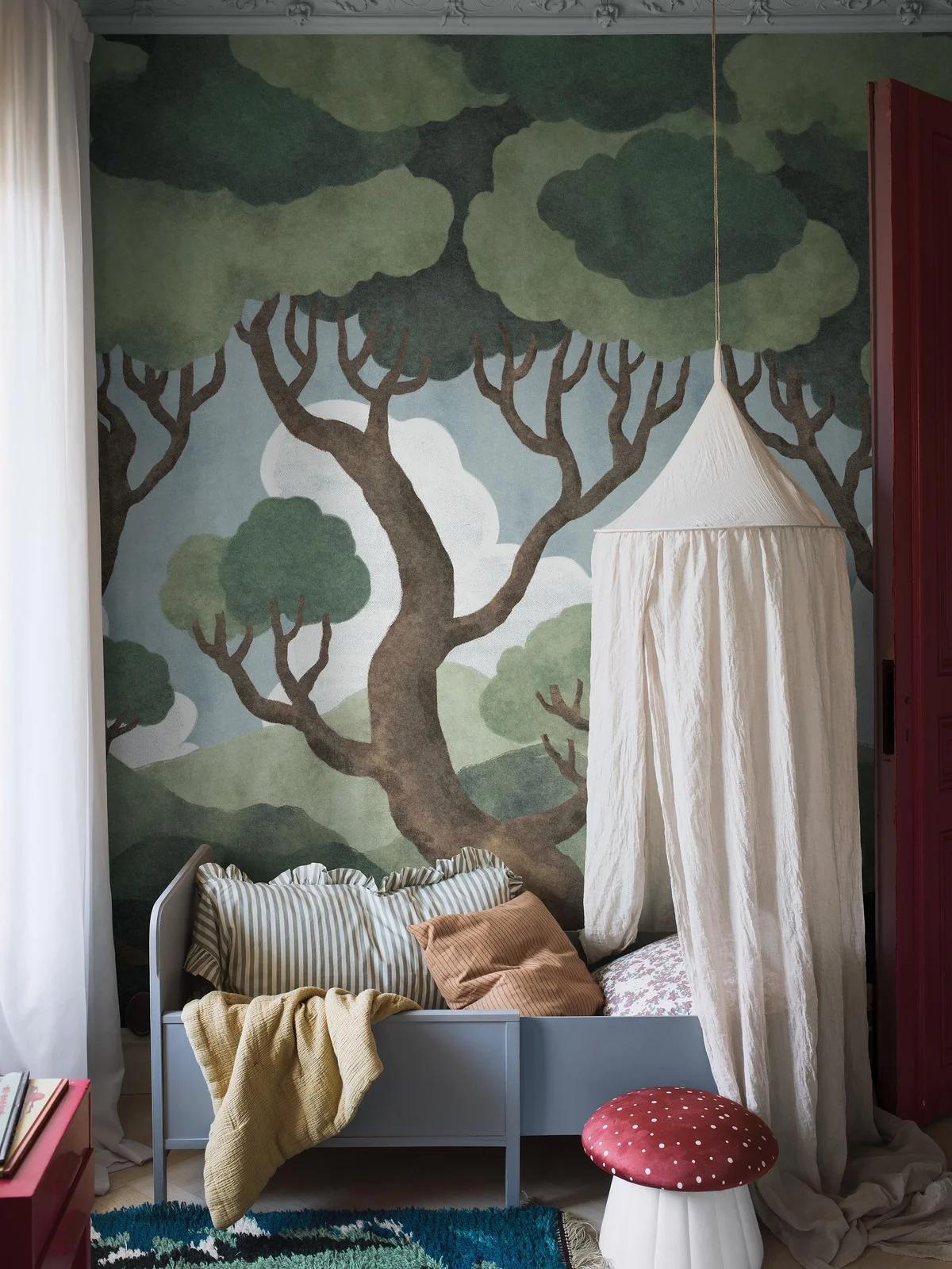 A cozy children's room featuring a forest mural, a grey daybed under a canopy, and a red mushroom stool.