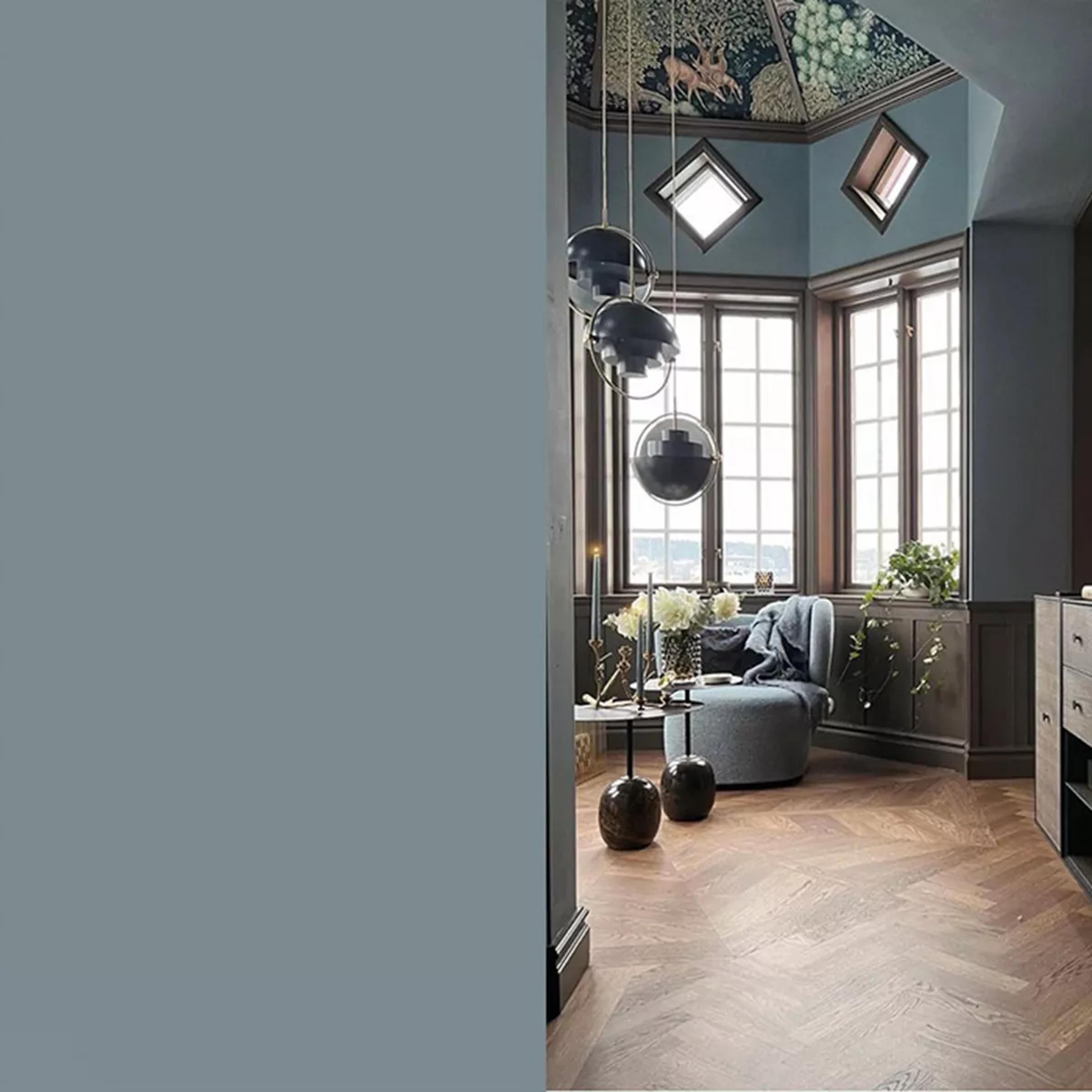 An elegant room with a forest mural ceiling, bay windows, modern pendant lights, a blue armchair, and herringbone floor.