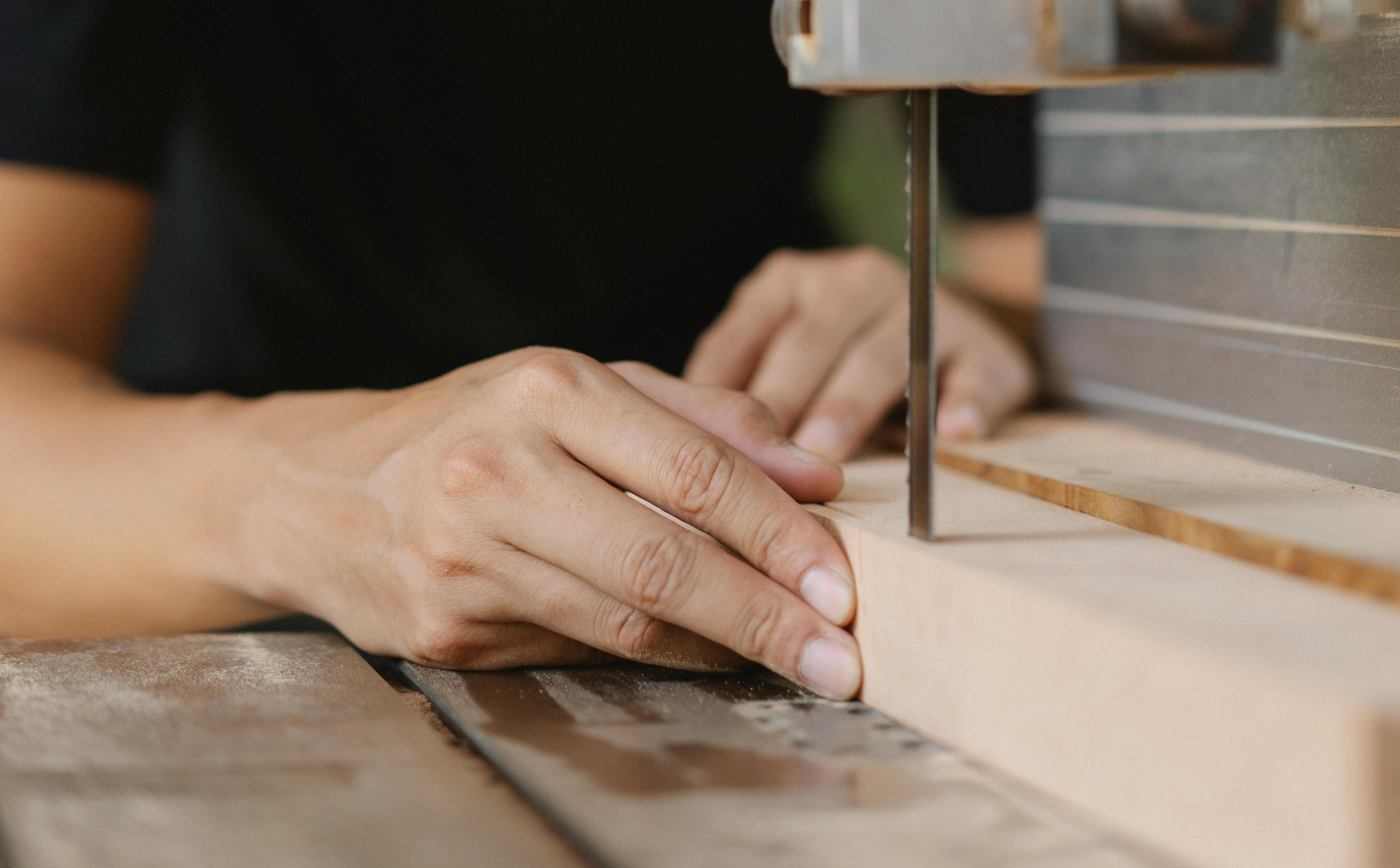 Hands cutting wood with a band saw.