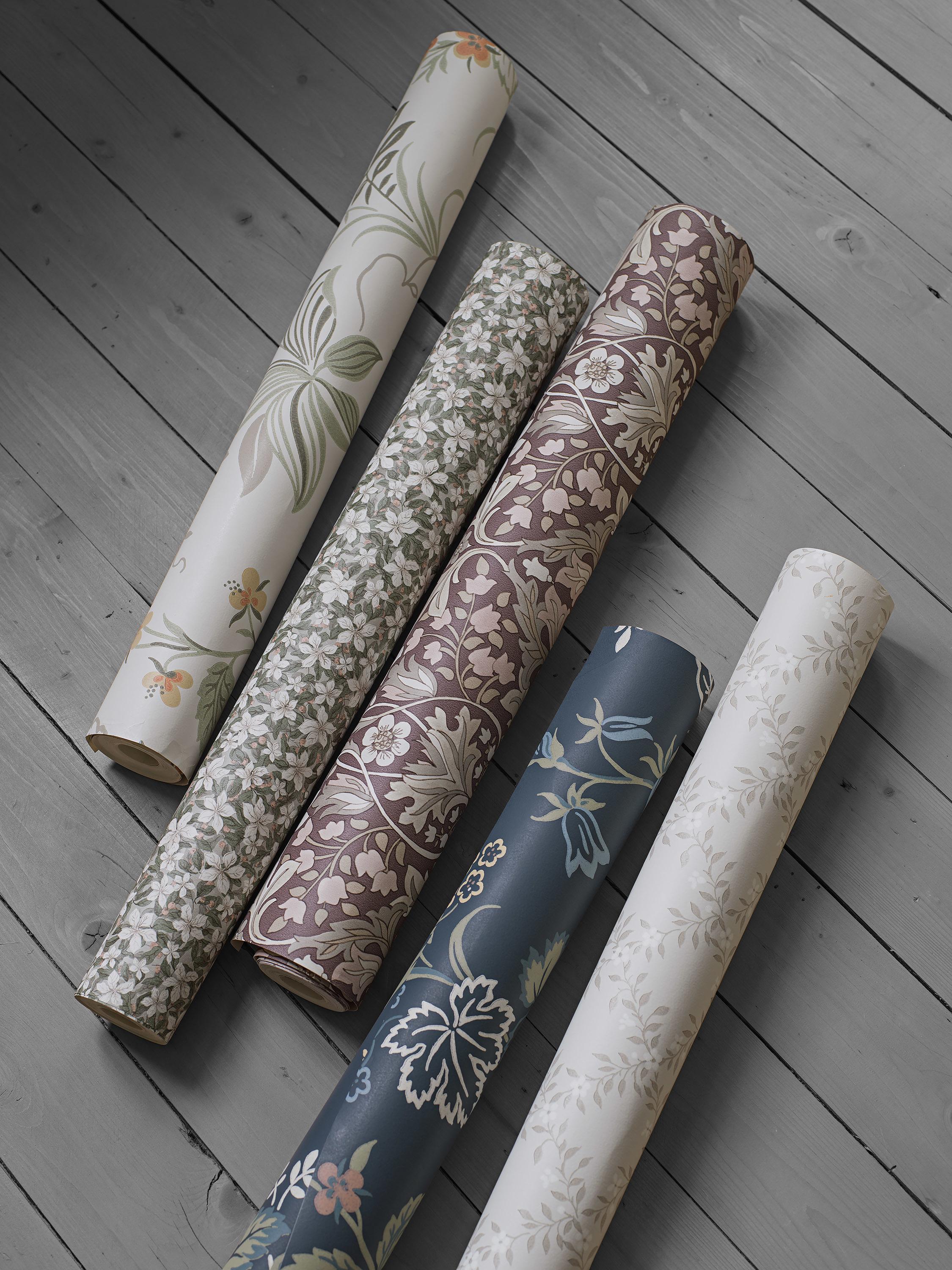 Six rolls of patterned wallpaper with floral designs on a wooden floor.
