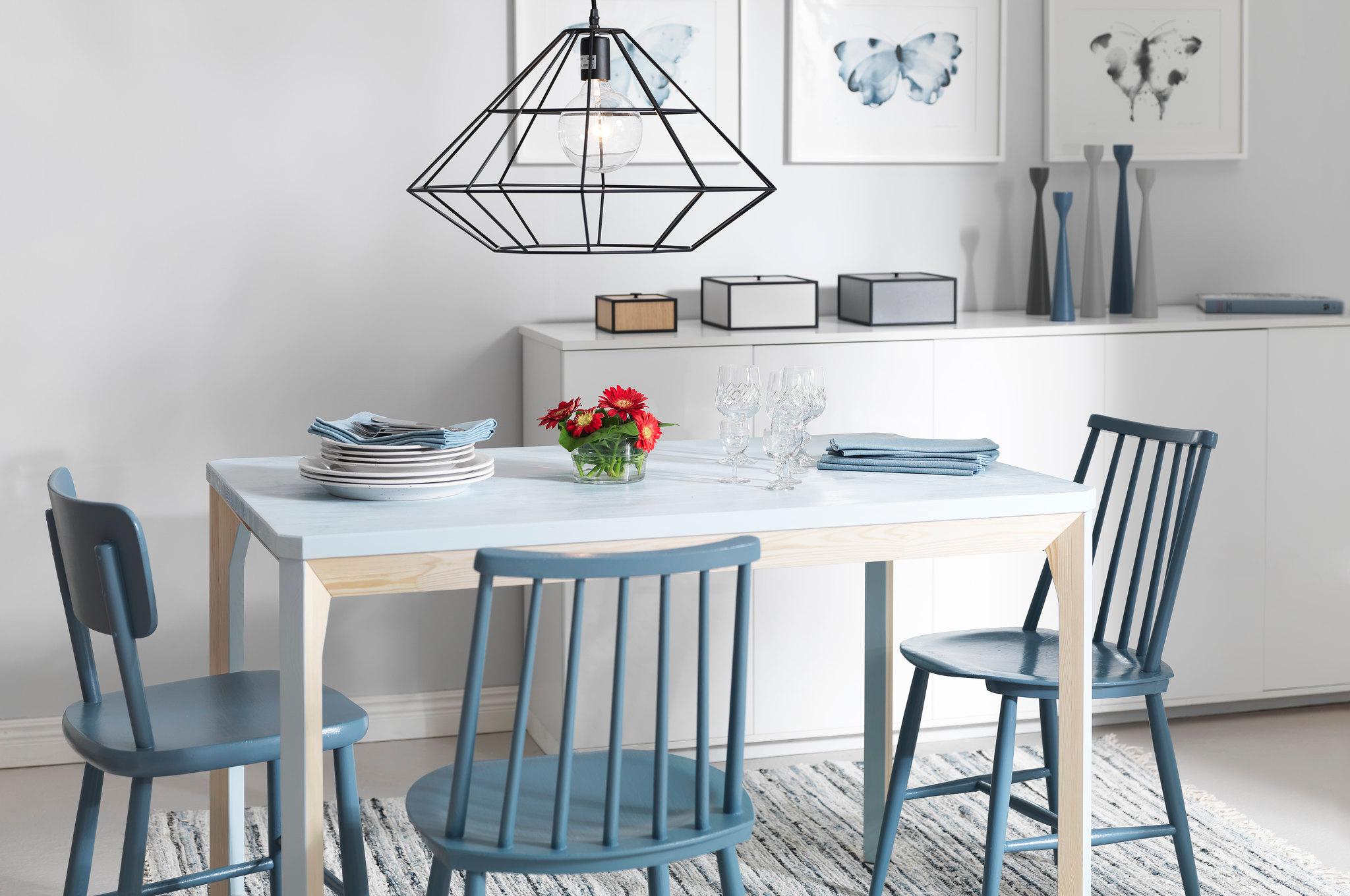 A dining room with a light blue table, three blue chairs, a black geometric pendant light, and three framed butterfly prints on the wall.