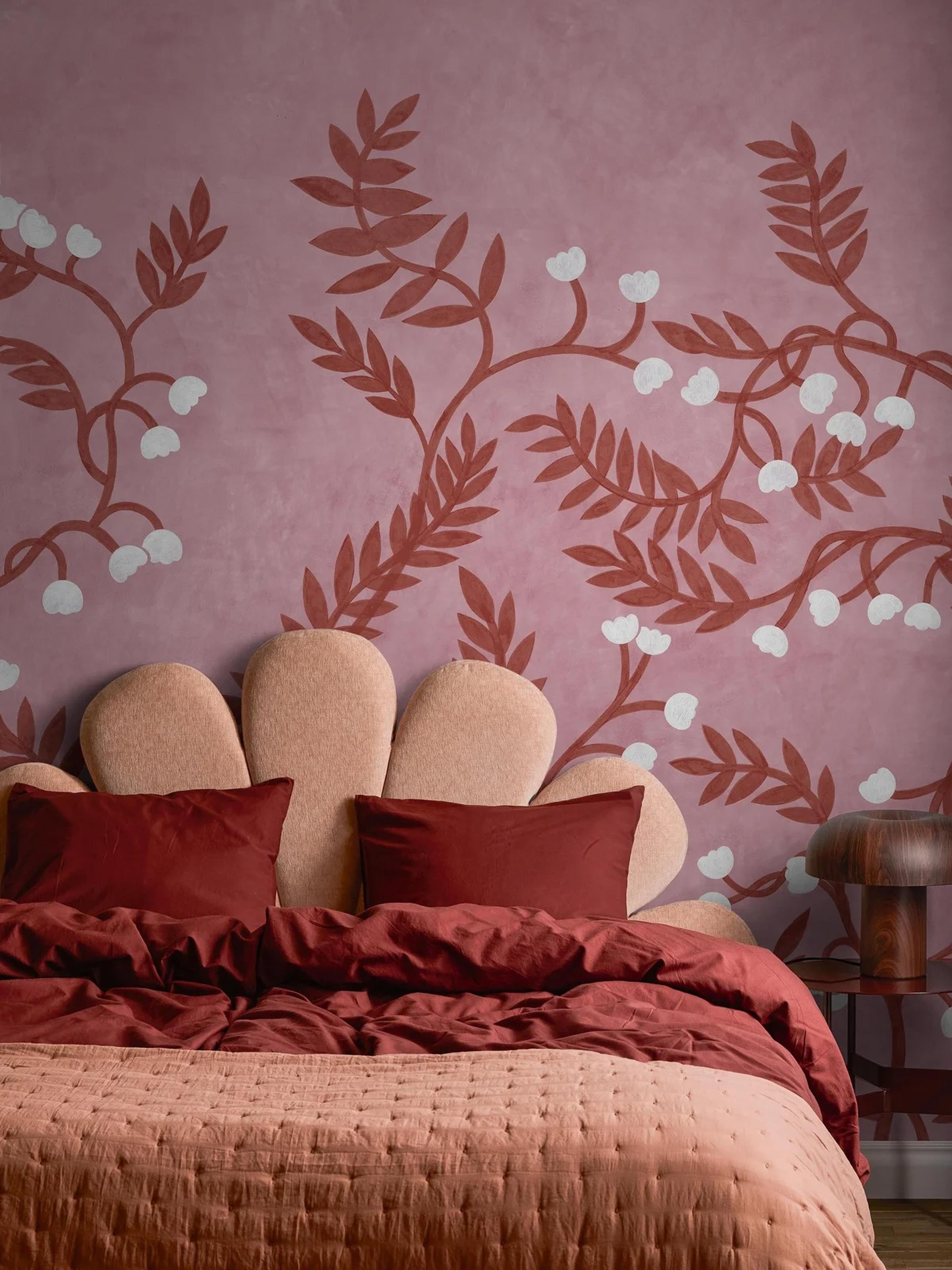A bedroom with a pink floral wall mural above a bed with a scalloped headboard and red and pink bedding.