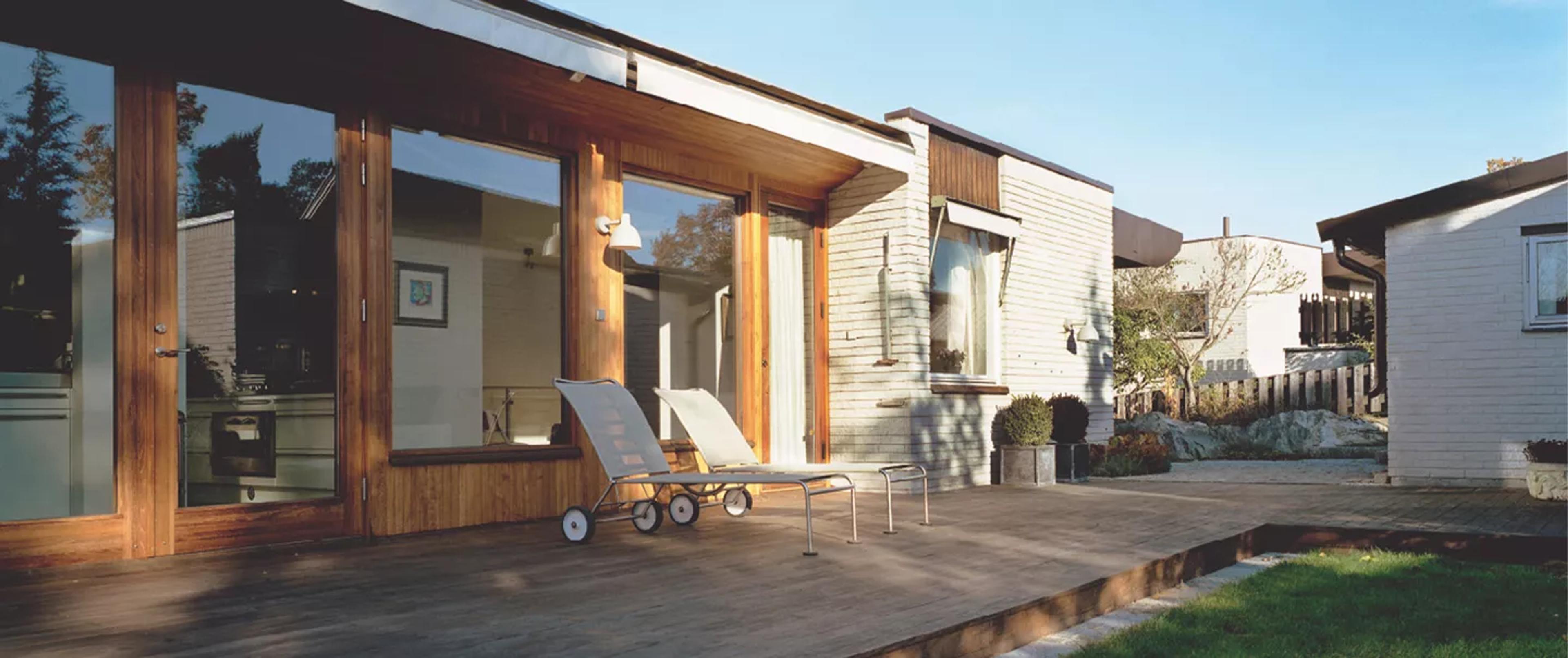 A modern house with a wooden deck and two lounge chairs under a sunny sky.