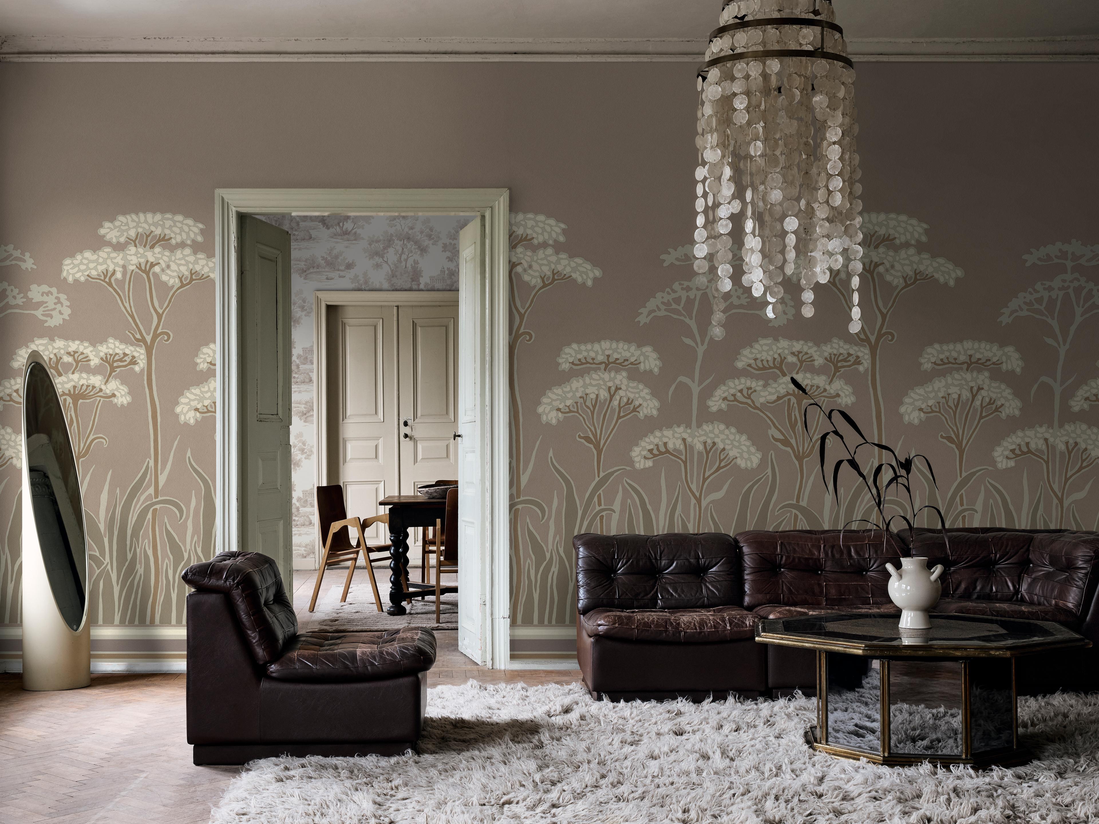 A living room with taupe wallpaper featuring a white botanical pattern, brown leather seating, a white shag rug, and a shell chandelier.