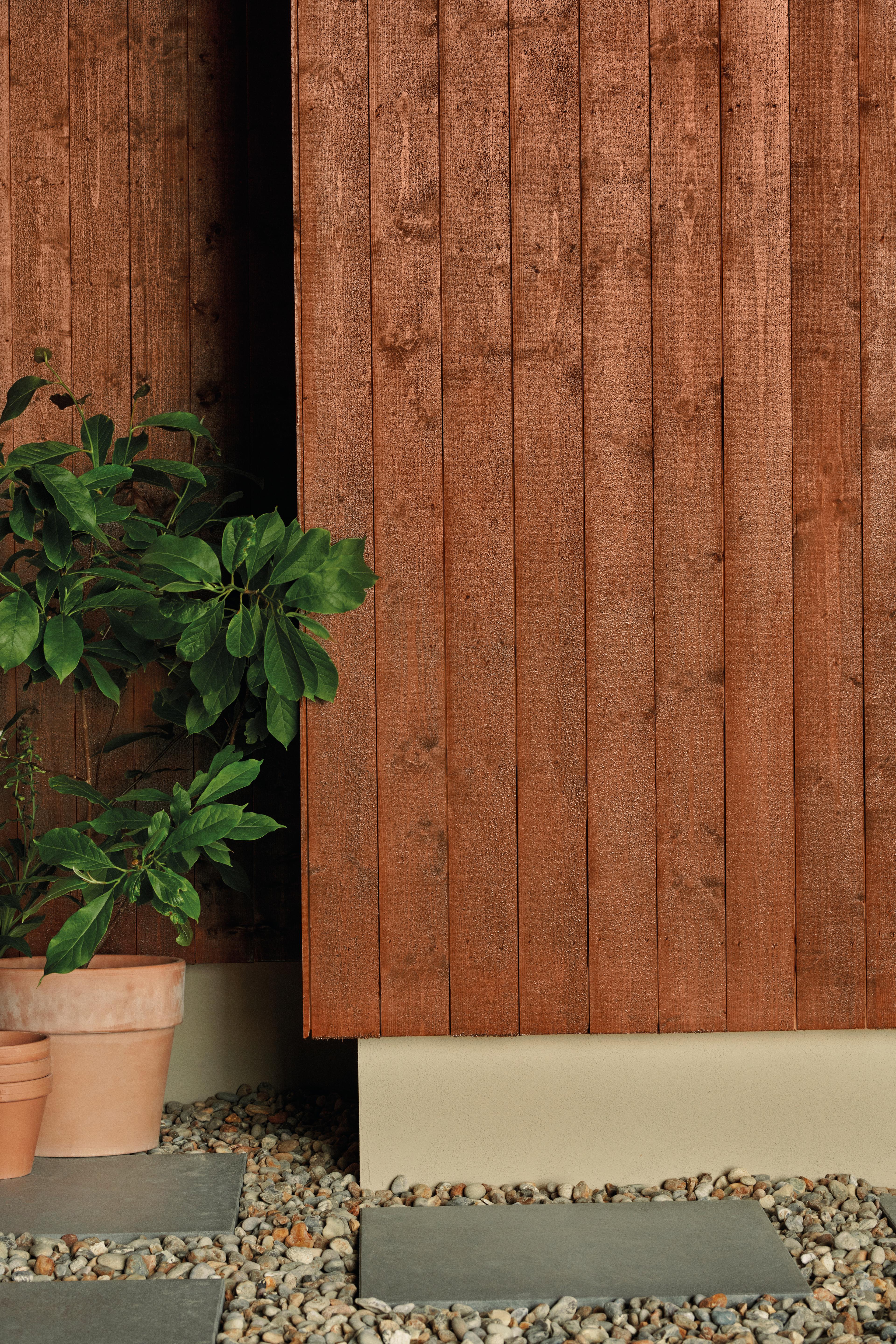 Reddish-brown wooden fence with a potted plant, gravel, and grey stepping stones.