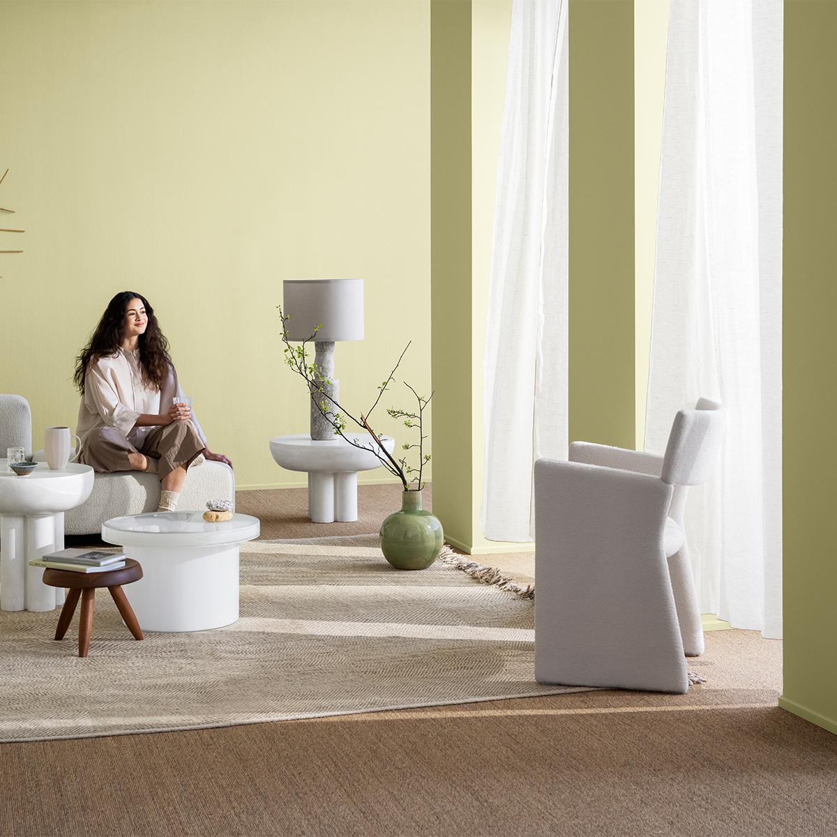 A woman sits relaxed in a modern living room with pale green walls and sculptural furniture.