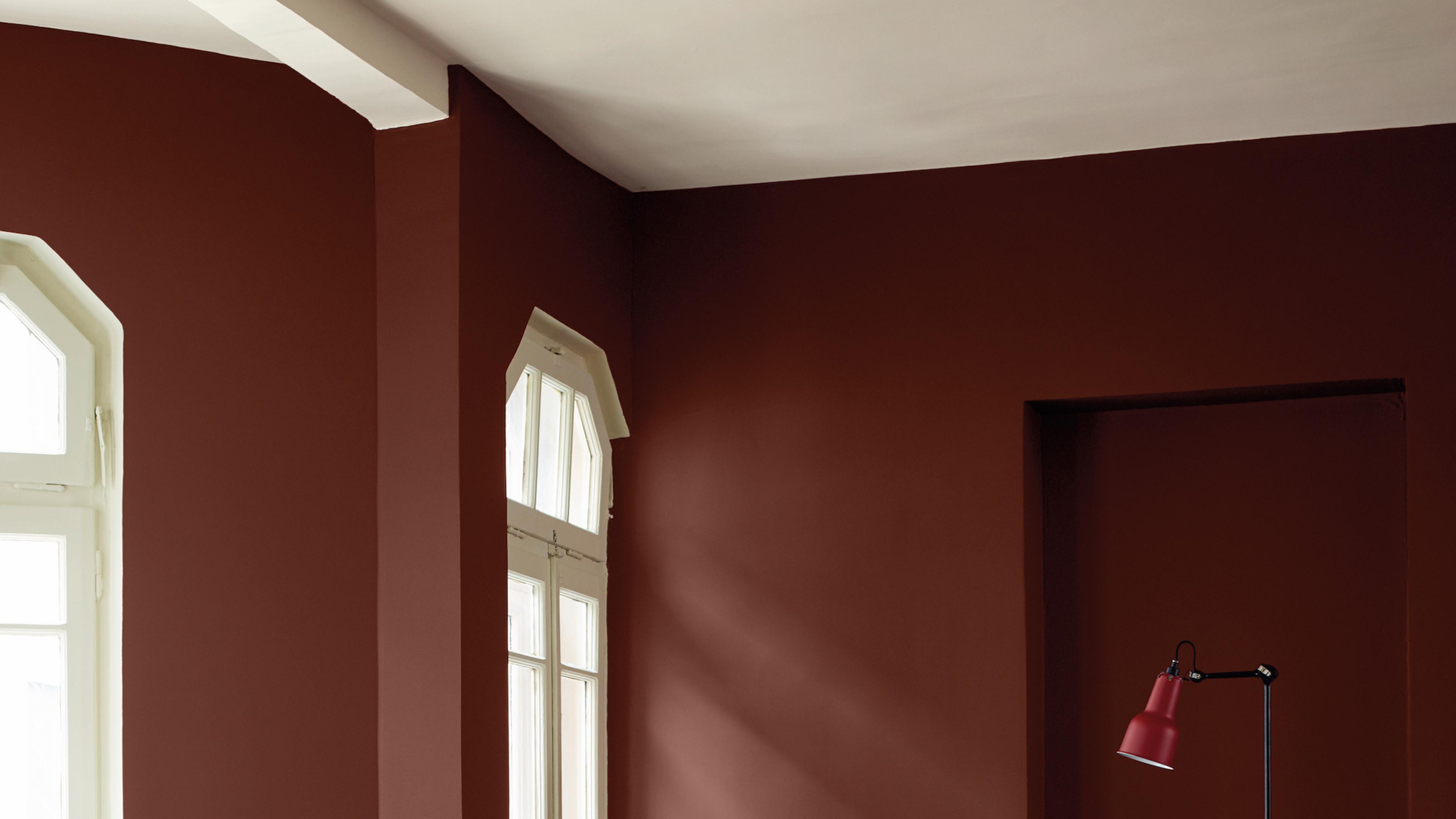 Room with deep reddish-brown walls, two white arched windows, and a red lamp.