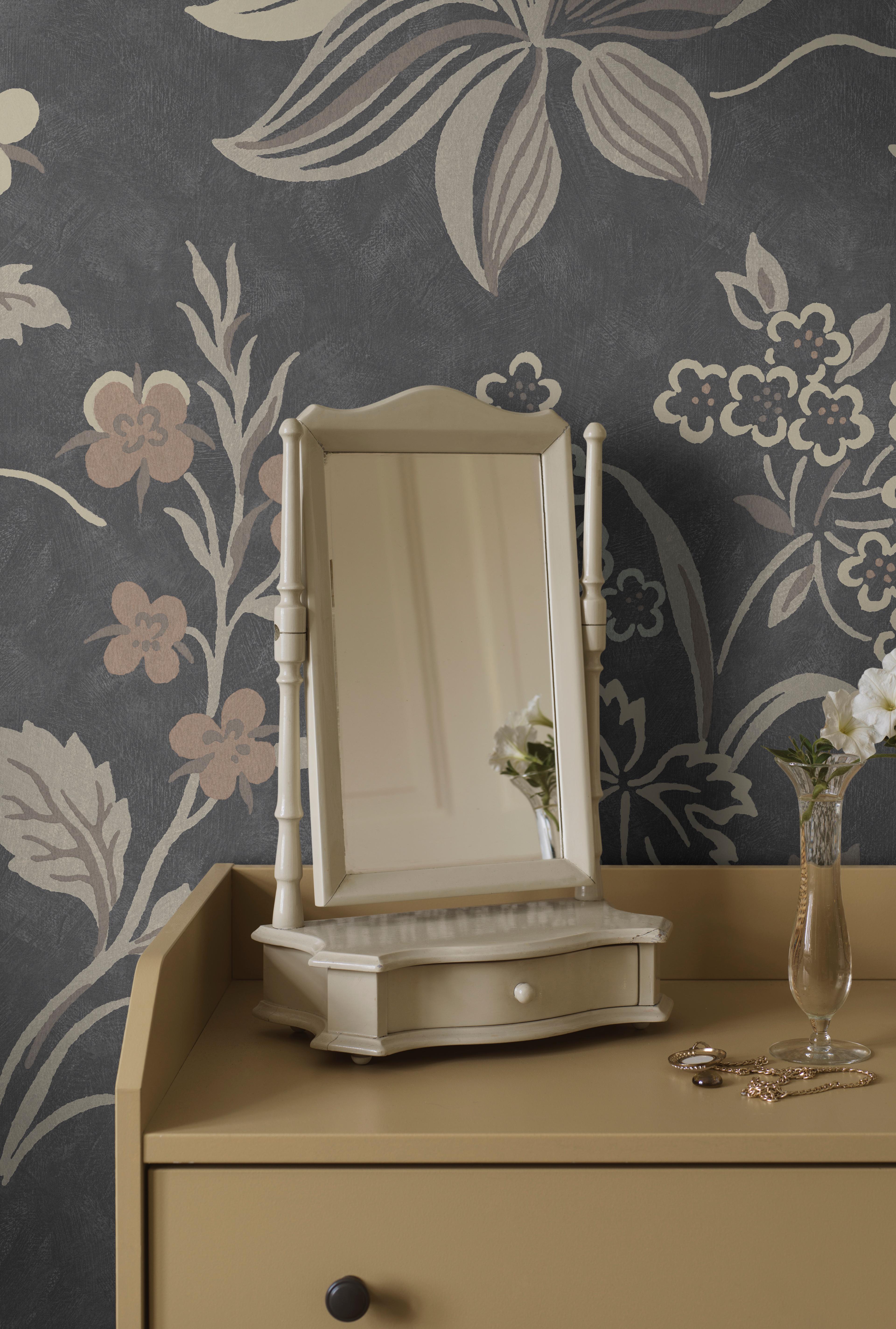 Cream vanity mirror on a beige dressing table against a dark gray floral wallpaper, with a vase of white flowers and jewelry.
