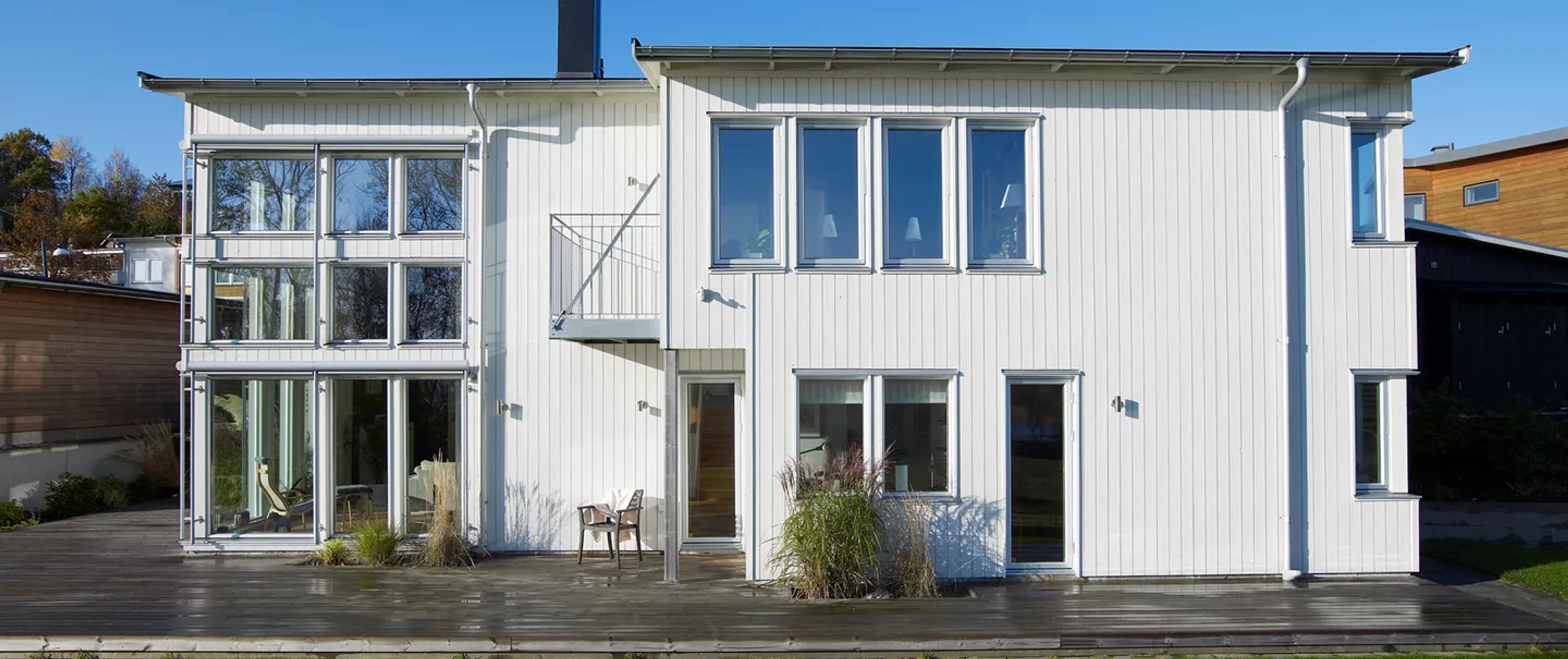 A modern, white two-story house with a large wooden deck and many windows.