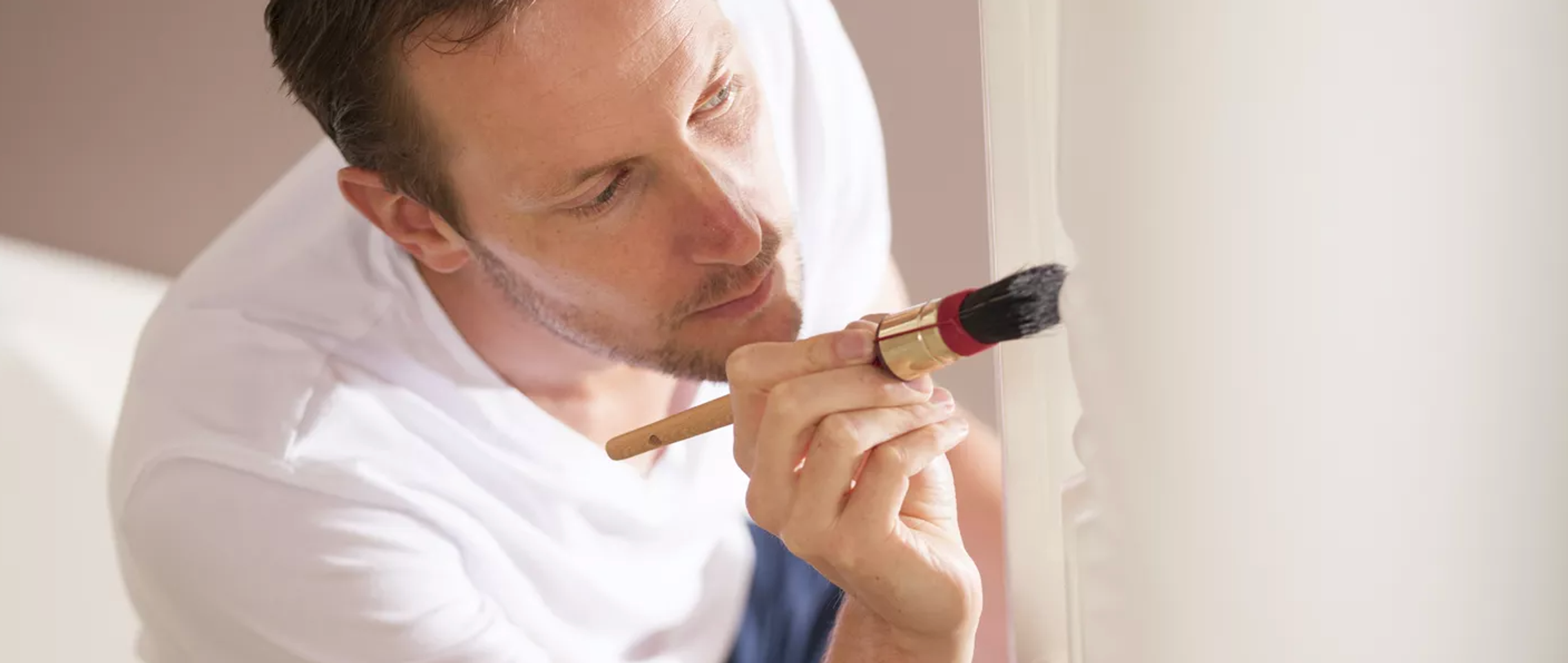 A man in a white shirt carefully paints a wall with a brush.