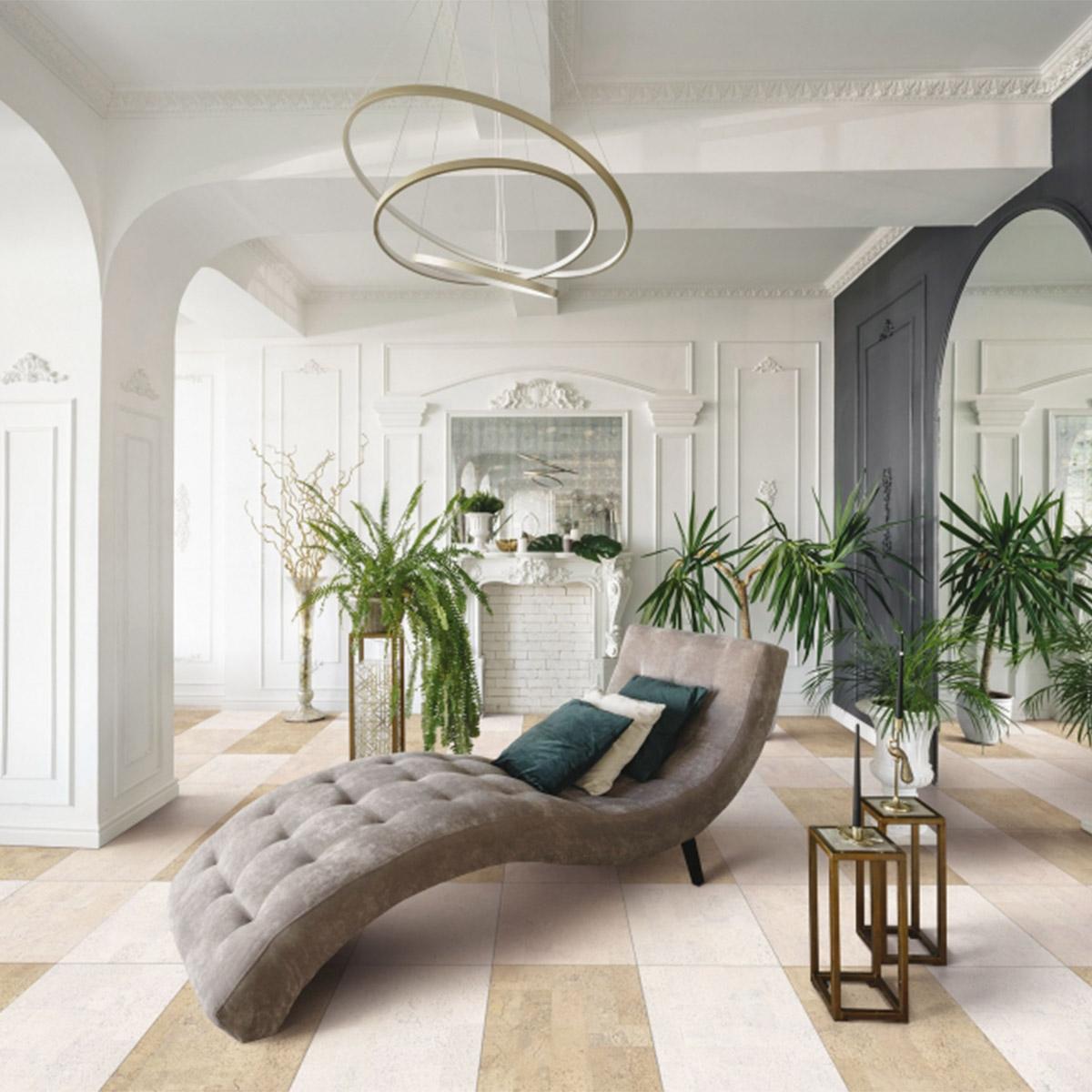 A stylish room with a gray chaise lounge, many plants, a modern chandelier, and a beige and cream checkered floor.