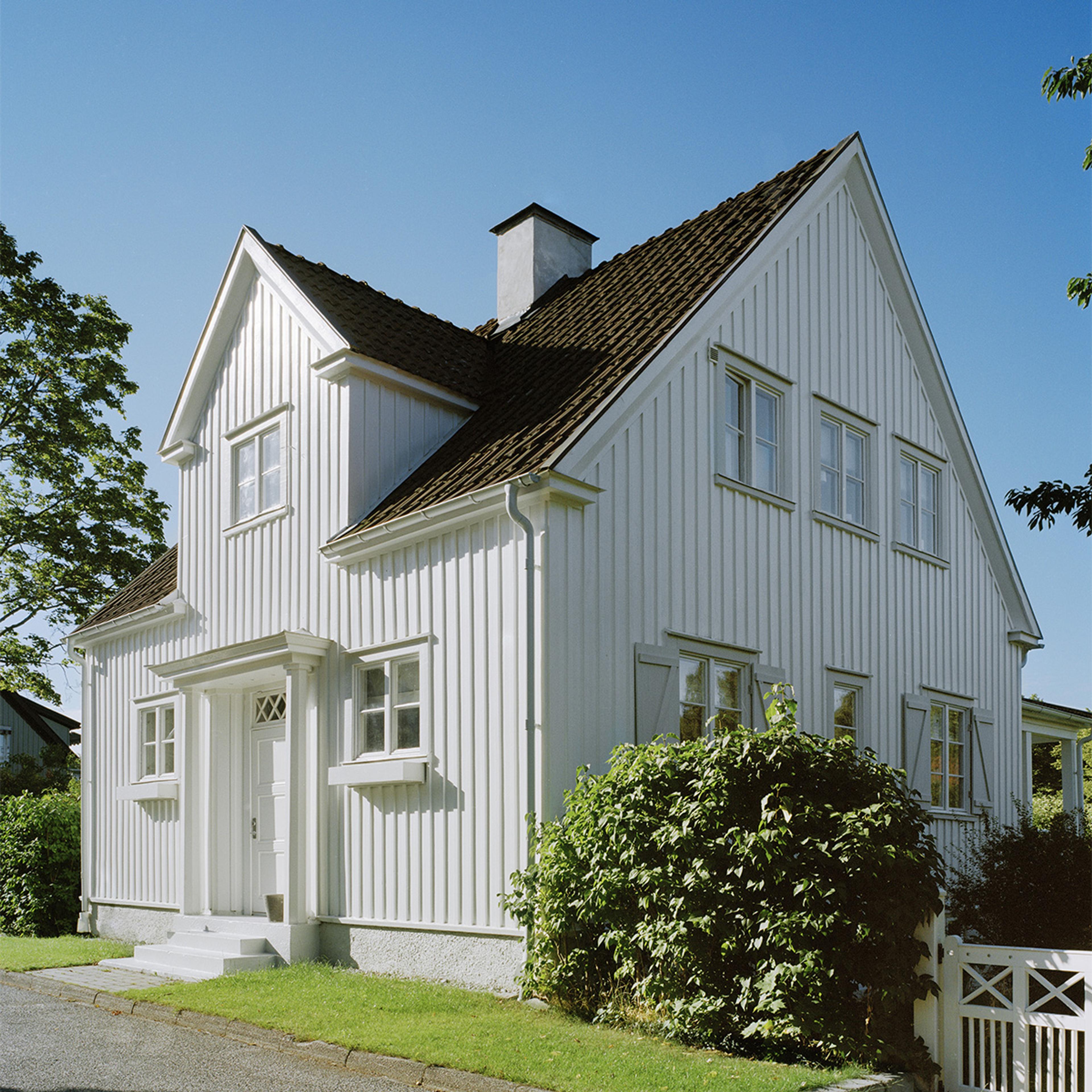 A white two-story house with vertical siding and a brown roof under a clear blue sky.