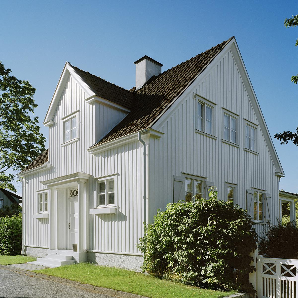 A white two-story house with vertical siding and a brown roof under a clear blue sky.