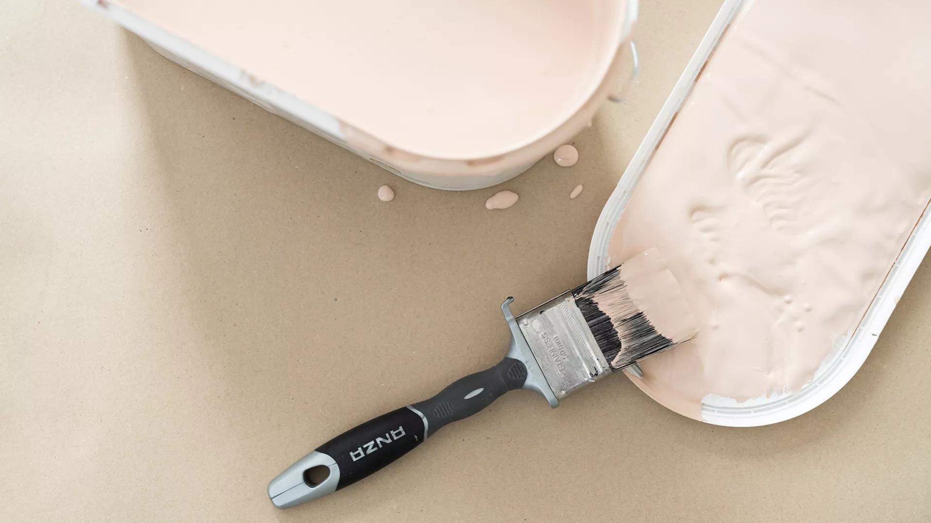 Paintbrush in a tray of pale pink paint, with another paint container nearby.