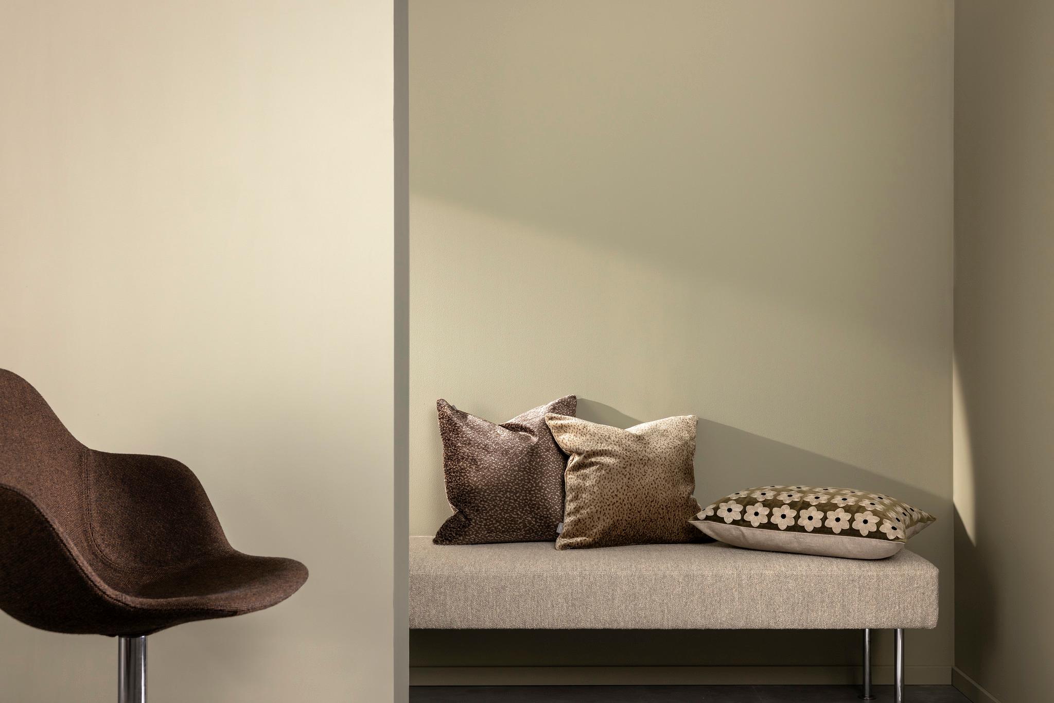 A modern room with a brown chair, a bench with pillows, and walls in muted beige and olive green.
