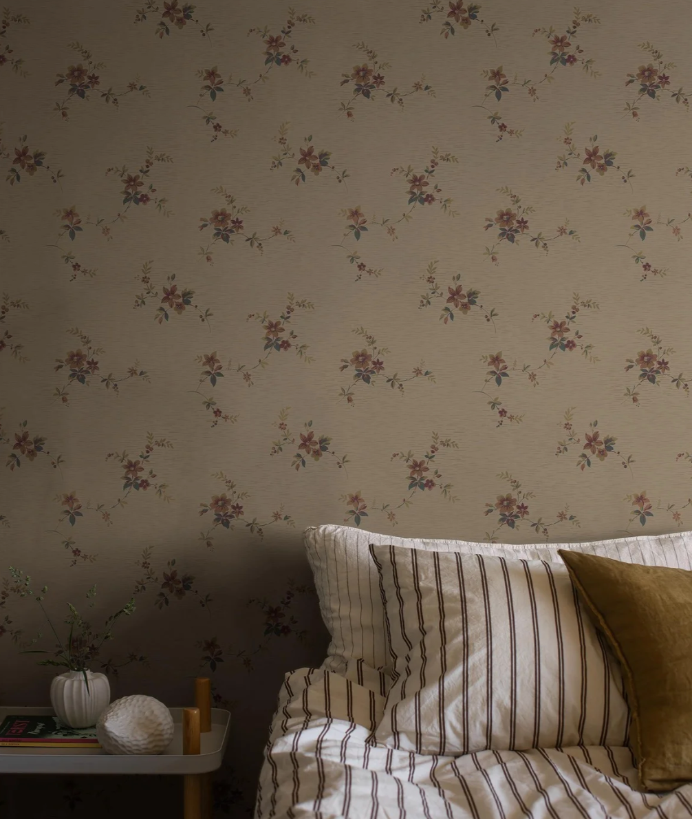 Floral wallpaper behind a bed with striped bedding and pillows, beside a small table.