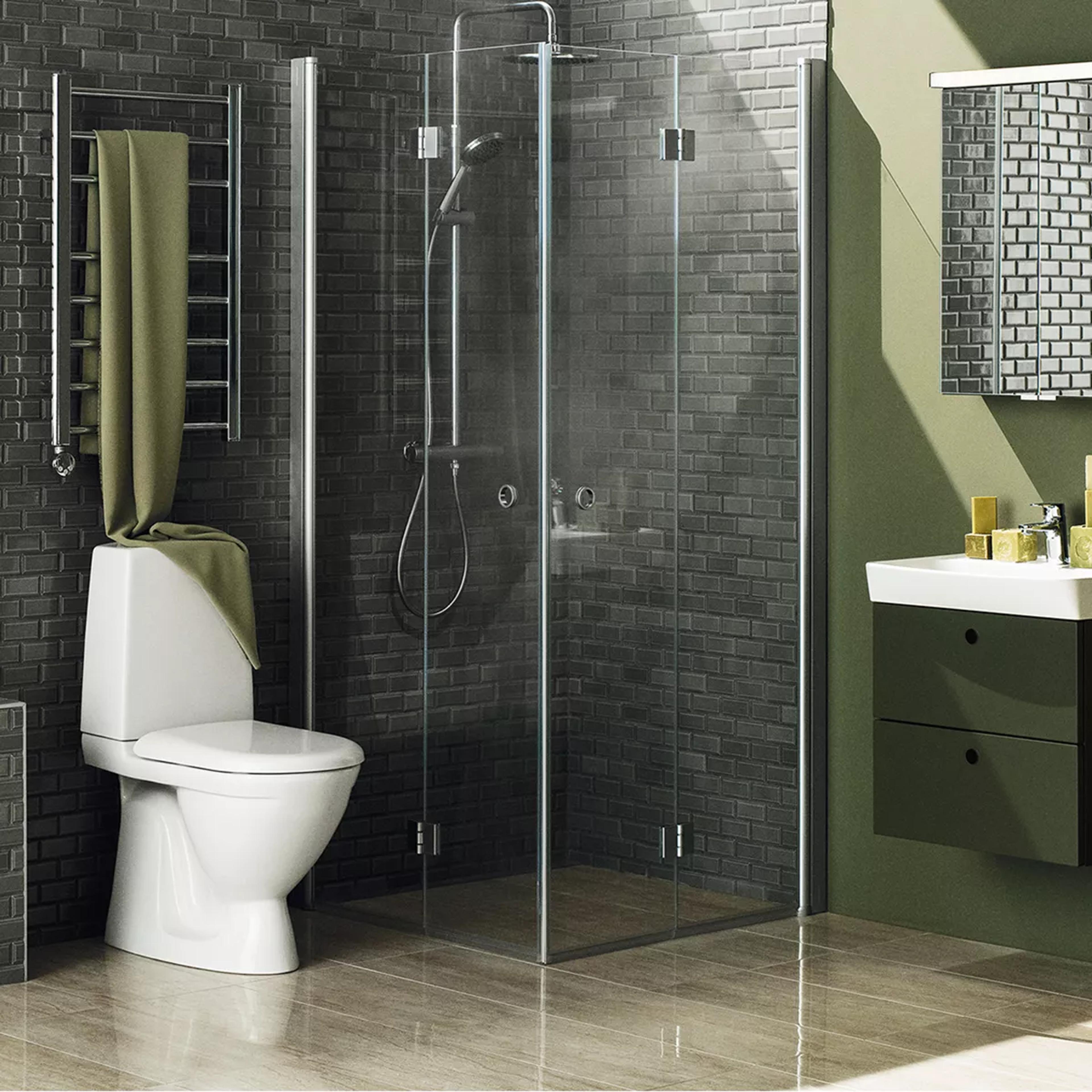 A modern bathroom with dark brick walls, a white toilet draped with a green towel, a glass shower enclosure, and a sink with a dark green vanity.