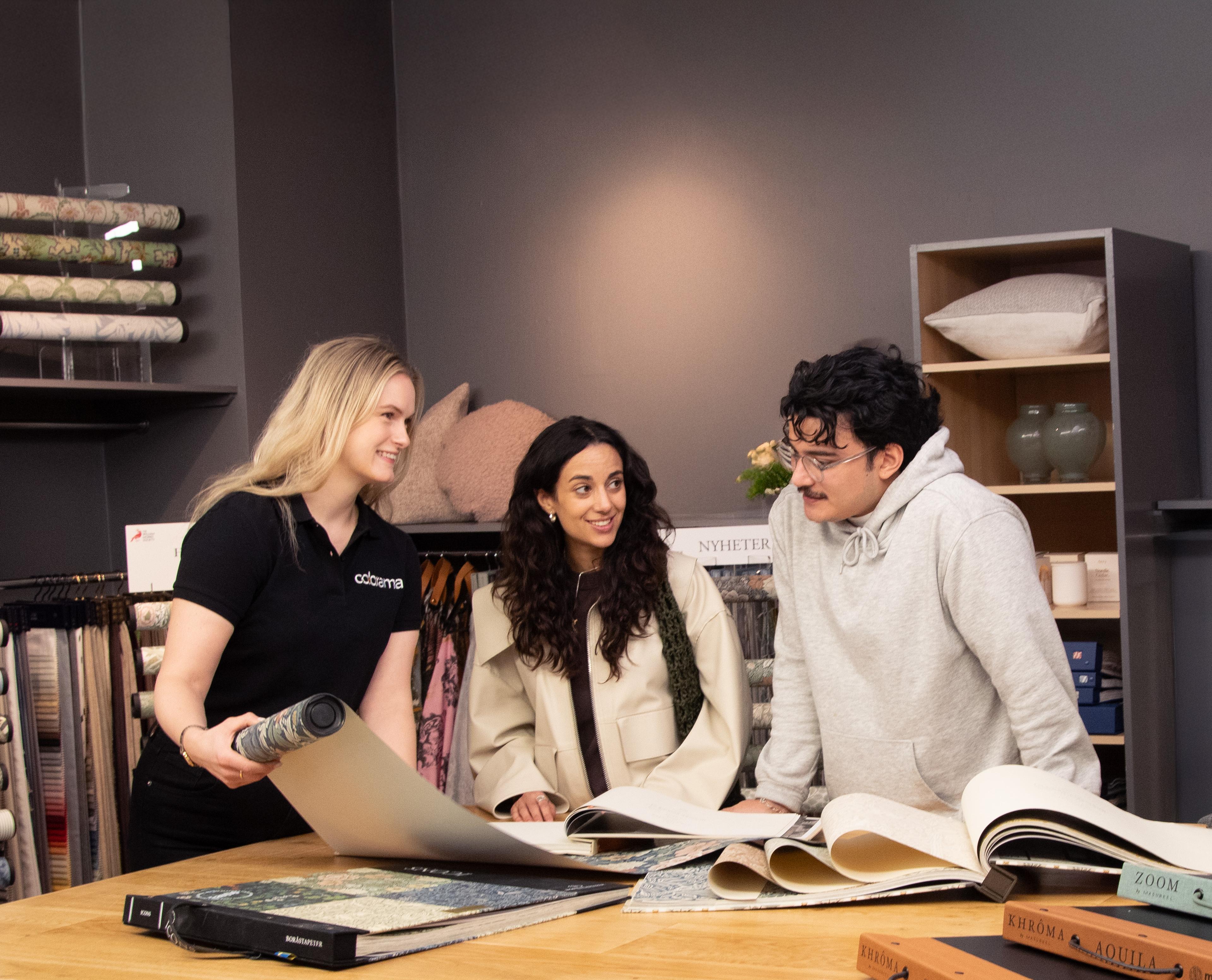 A store employee shows wallpaper samples to a smiling couple in a home decor store.
