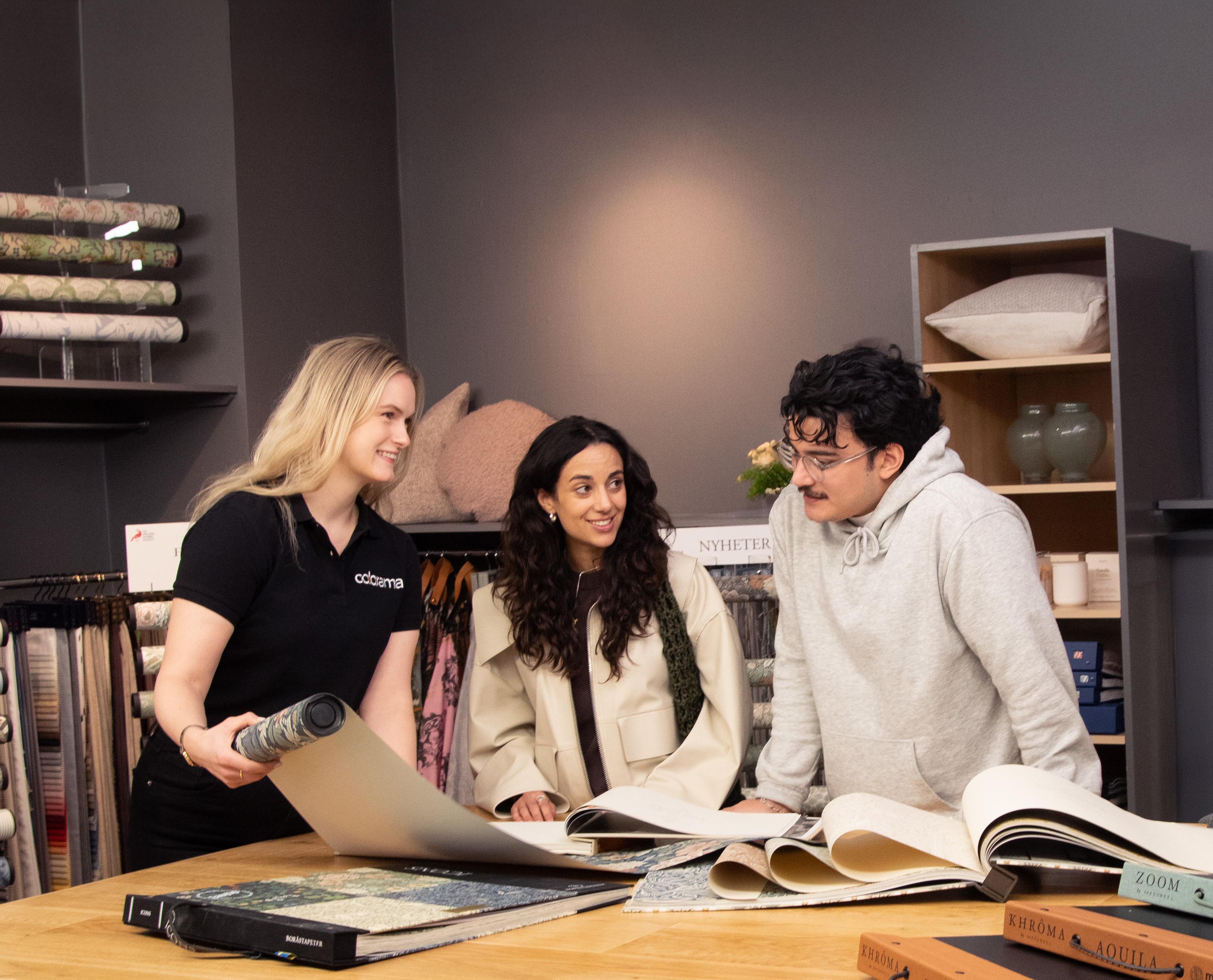A store employee shows wallpaper samples to a smiling couple in a home decor store.