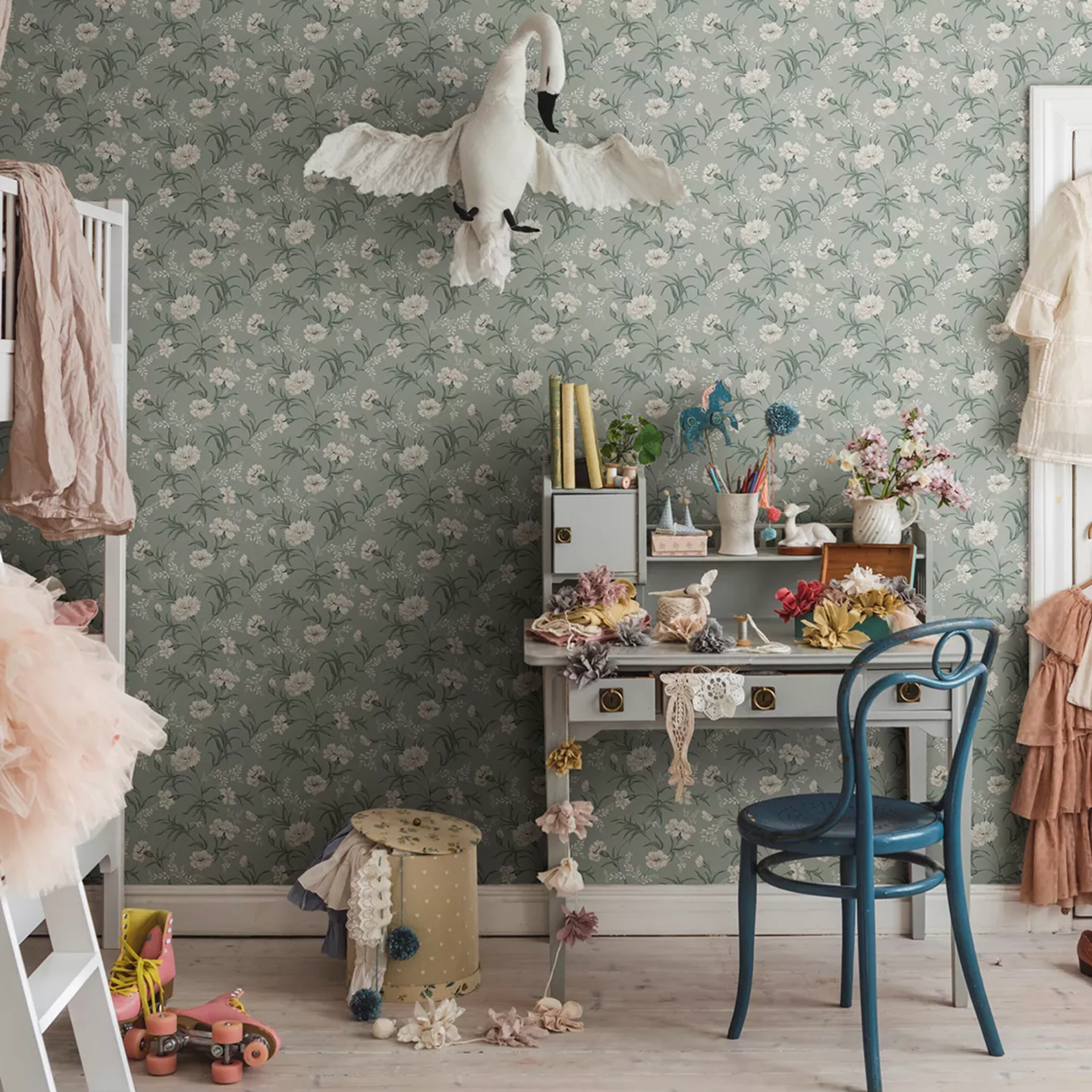 Whimsical child's room with green floral wallpaper, a fabric swan, craft desk, and pink roller skates.
