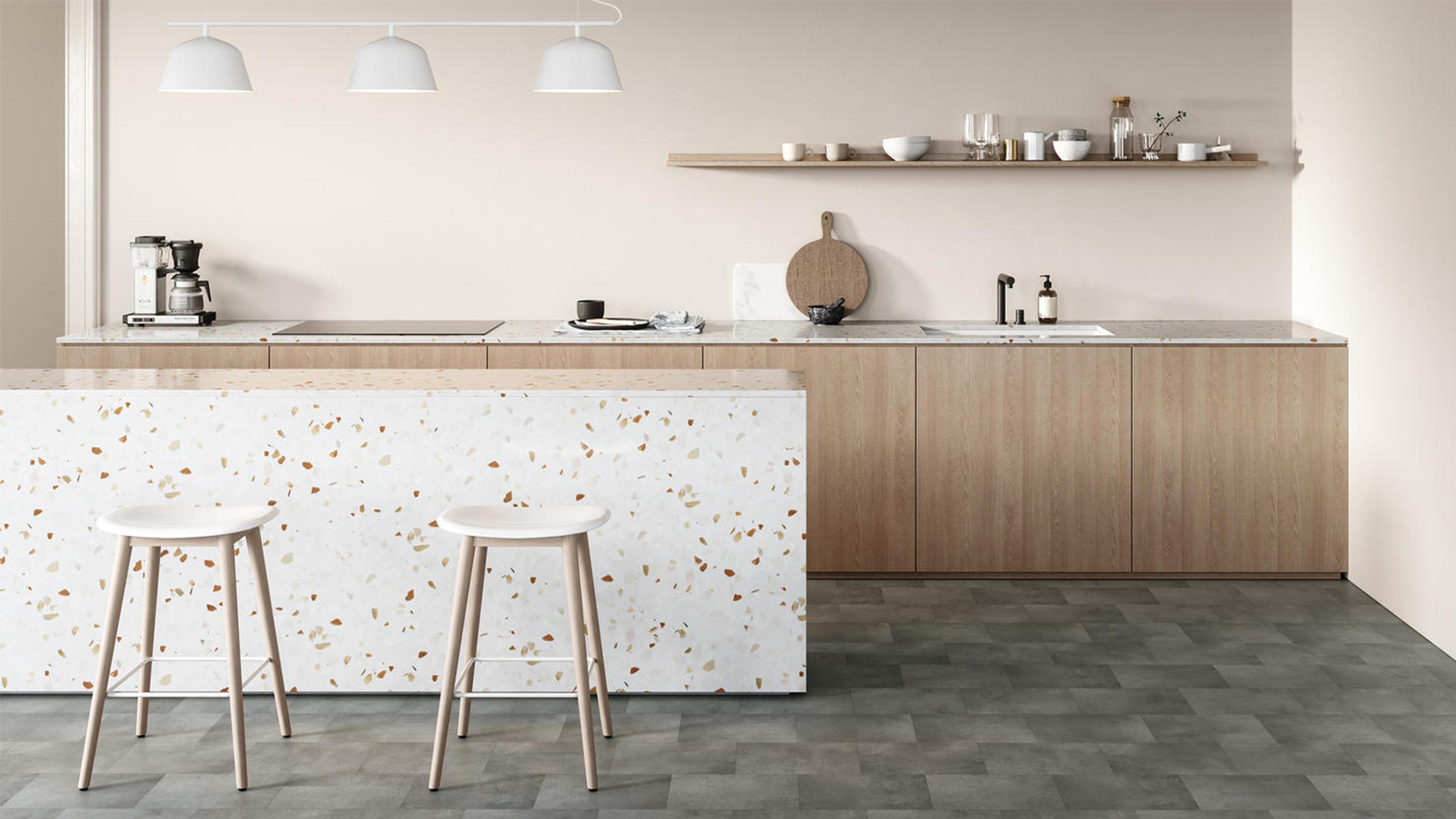 A modern kitchen with a terrazzo island, two bar stools, light wood cabinets, and an open wooden shelf.
