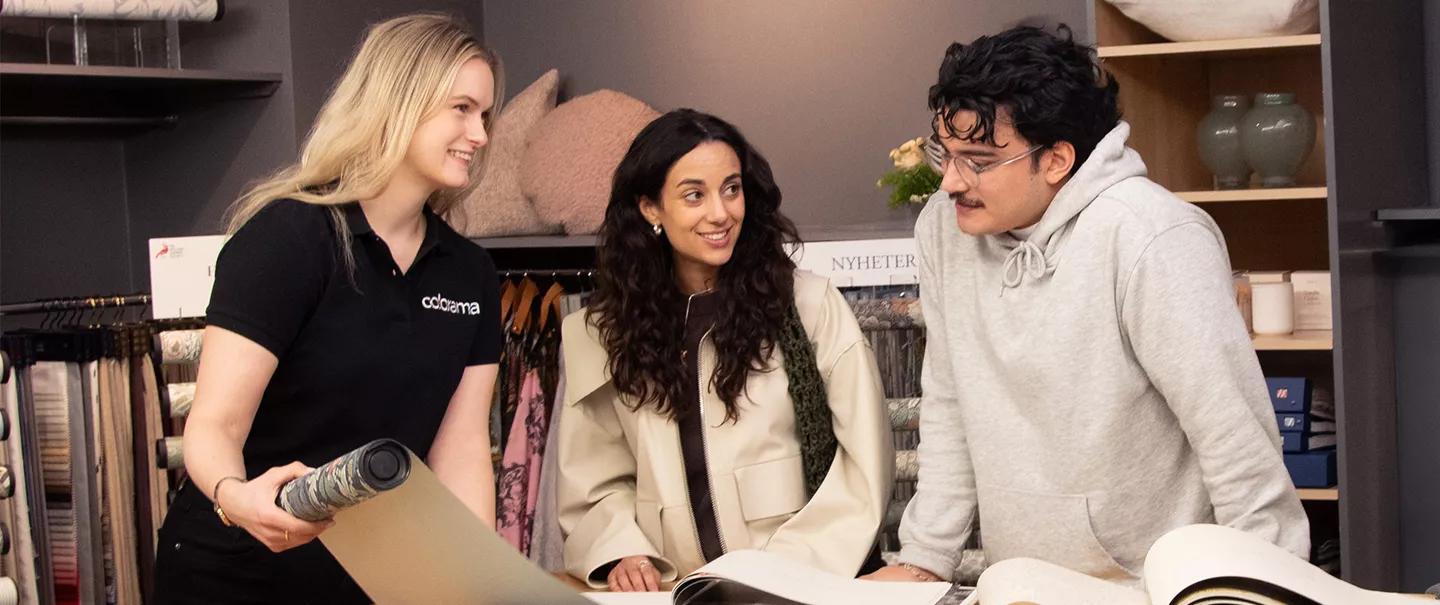 A sales associate shows wallpaper samples to a man and a woman in a store.
