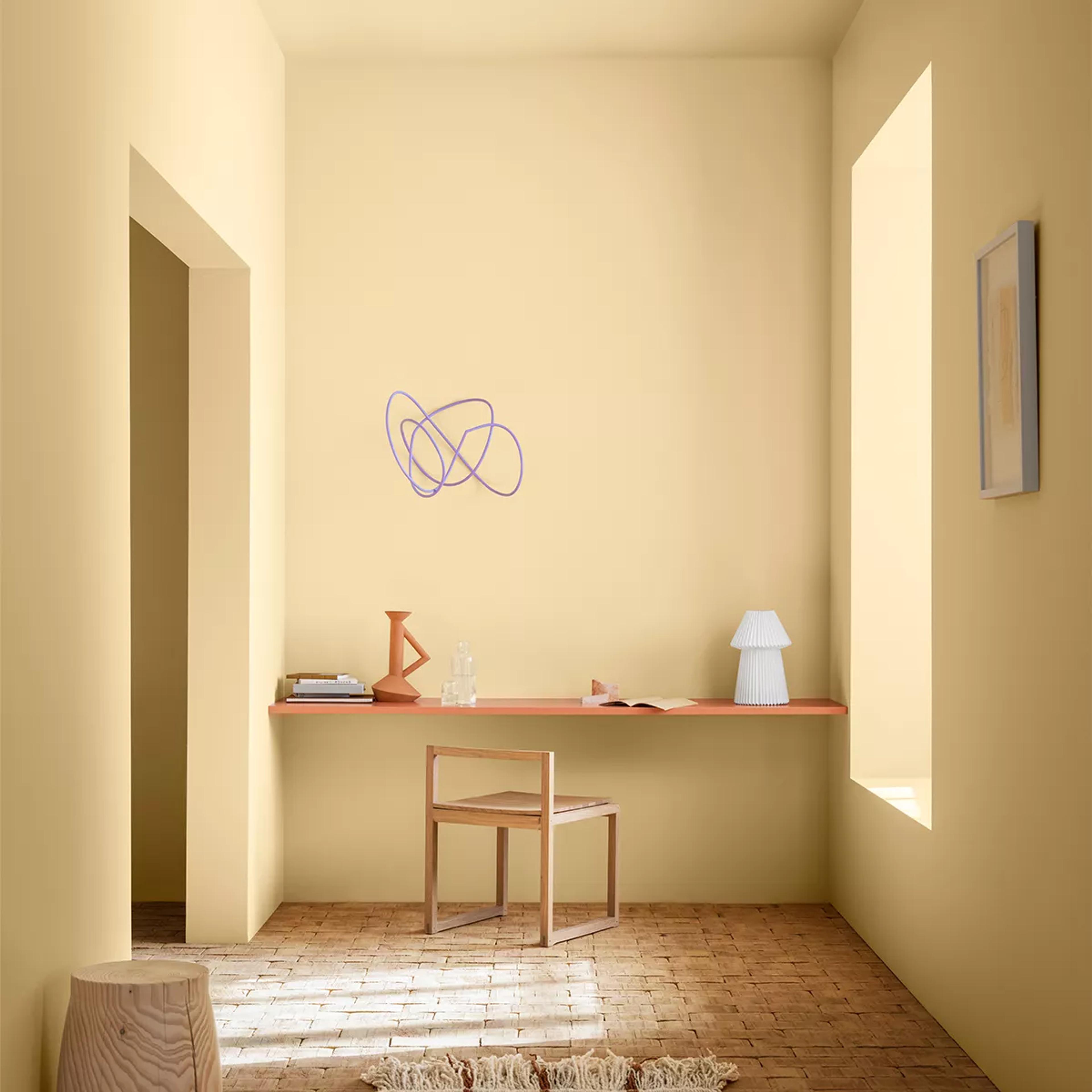 A minimalist pale yellow room with a floating orange-red desk, wooden chair, and abstract purple wall art.