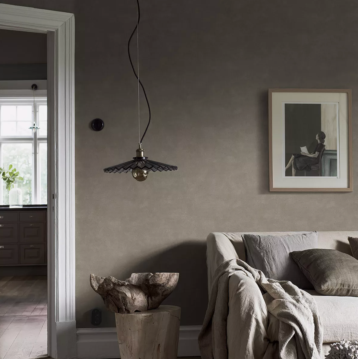 A neutral-toned living room featuring a pendant light, a sofa with a throw, and a wooden side table.
