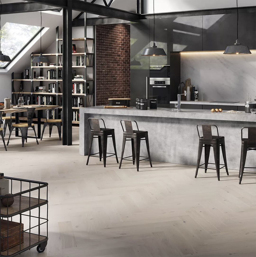 An open-plan industrial loft featuring light herringbone wood floors, a concrete kitchen island, and a dining area.