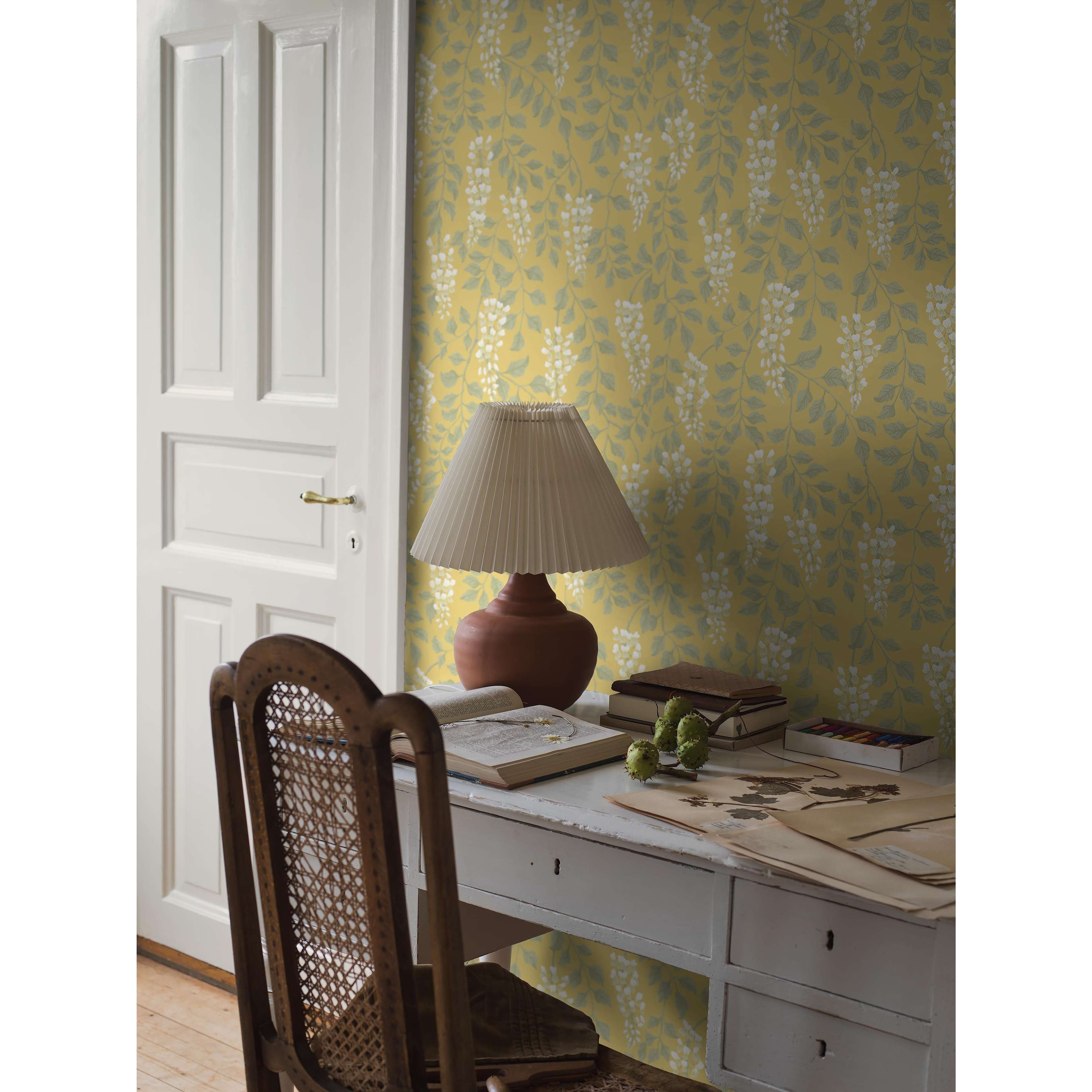 Blåregn gul, tapet tapet med botaniskt, blommigt mönster i gul. Från kollektionen Orangeri. Nonwoven-material med förskjuten passning. Passar i vardagsrum och kök.