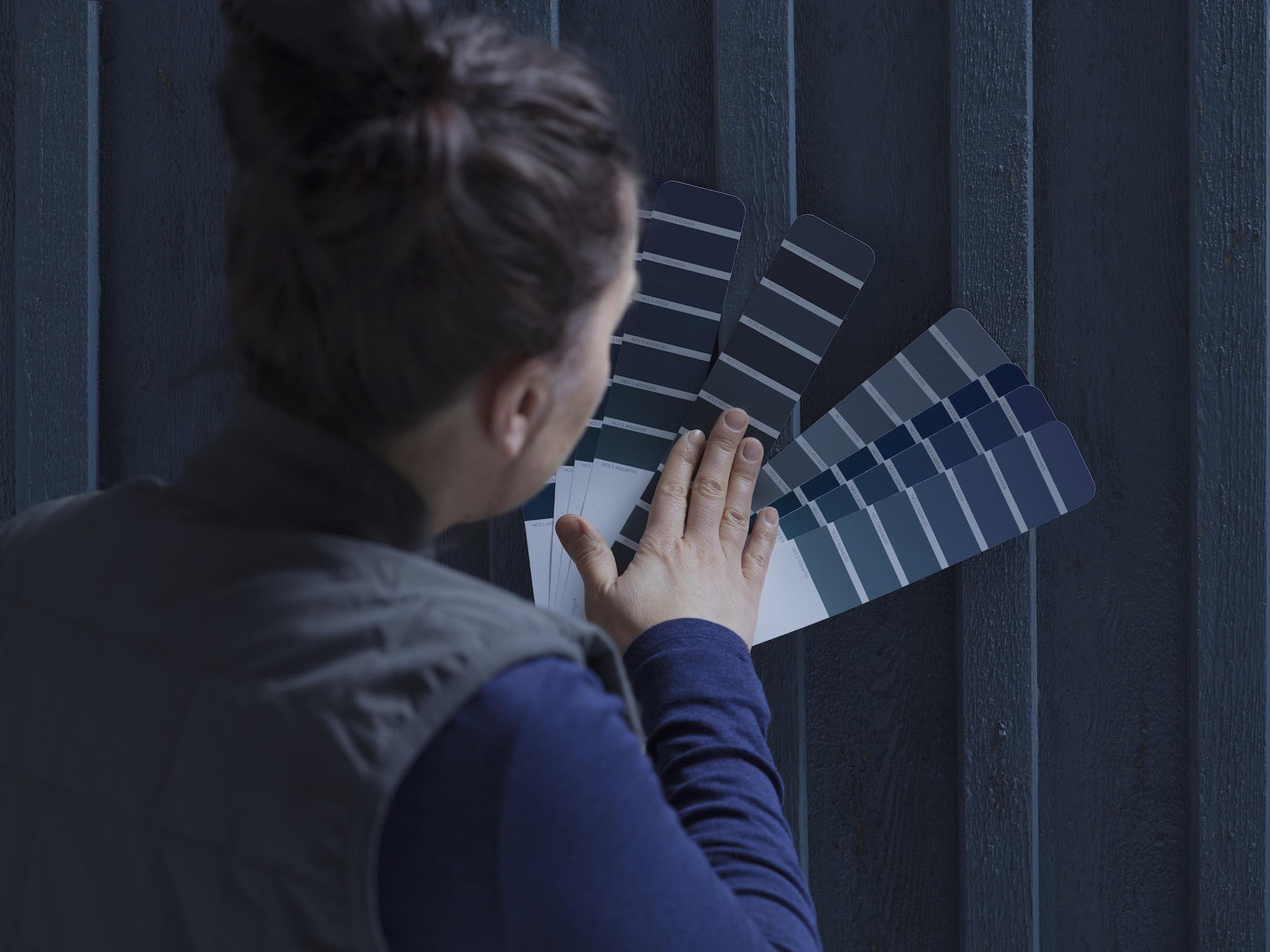 Person viewing blue and gray paint swatches against a dark wall.