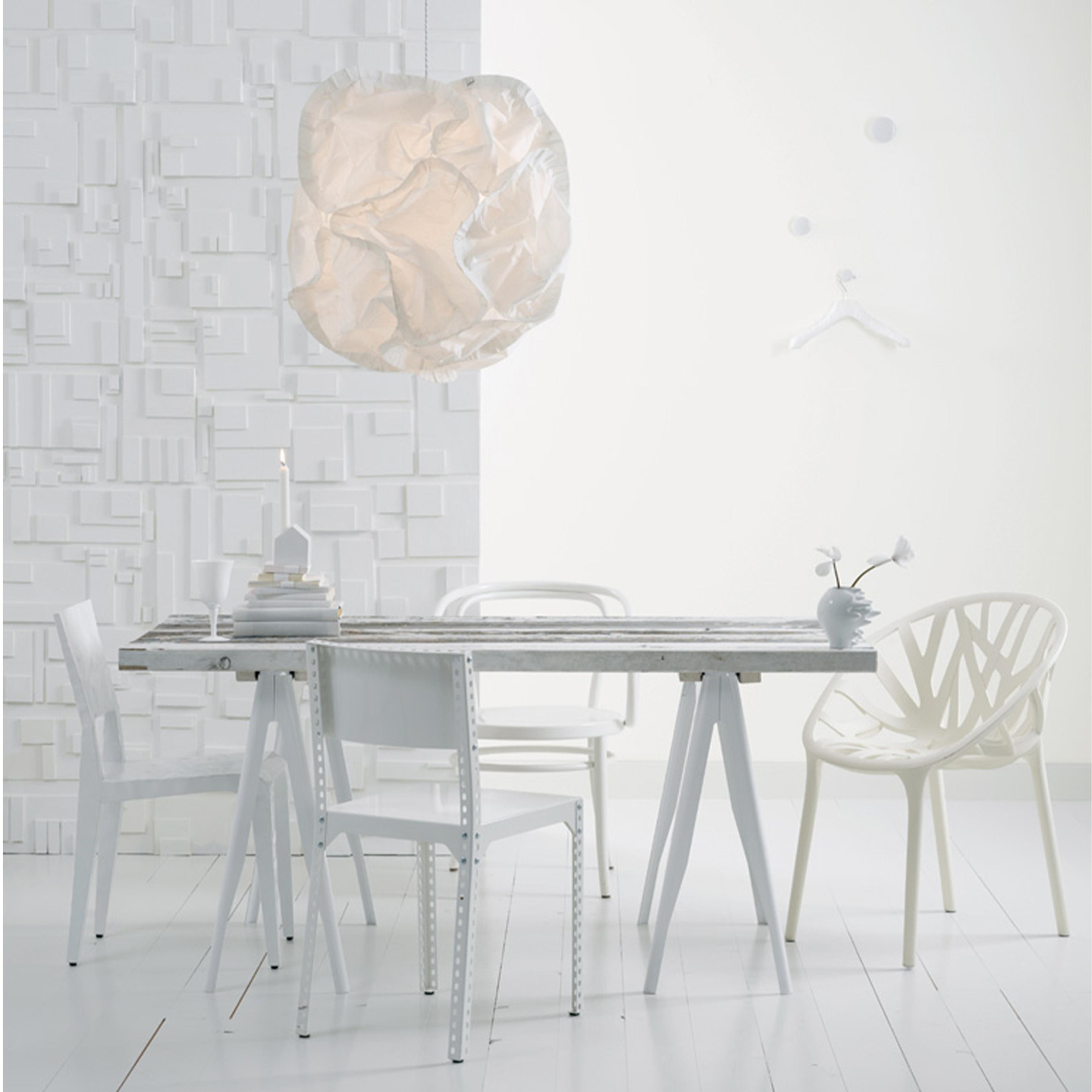 An all-white modern dining room with a long table, diverse chairs, a crumpled paper pendant lamp, and a textured wall.