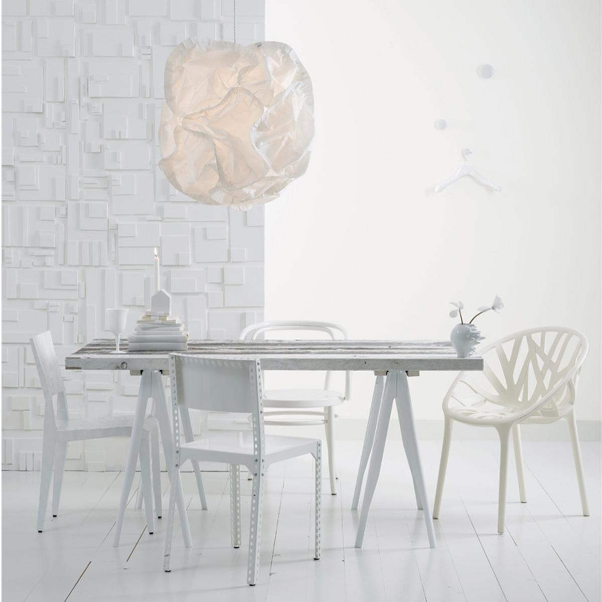 An all-white modern dining room with a long table, diverse chairs, a crumpled paper pendant lamp, and a textured wall.